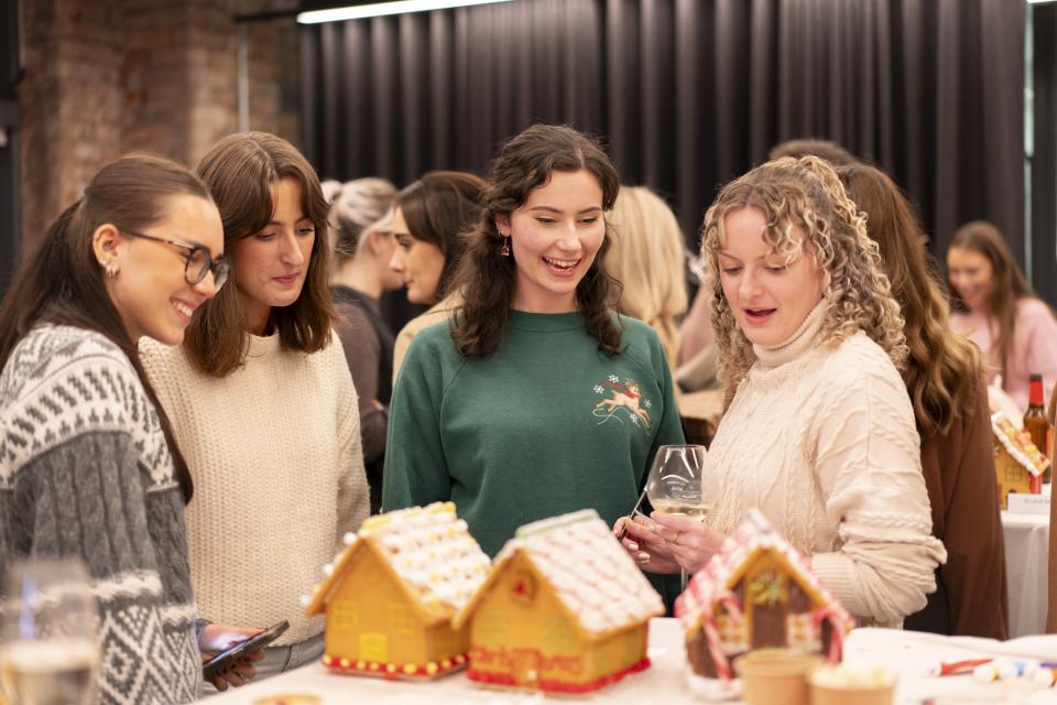 Women enjoying a festive celebration at Material Source Studio, admiring colorful gingerbread houses.