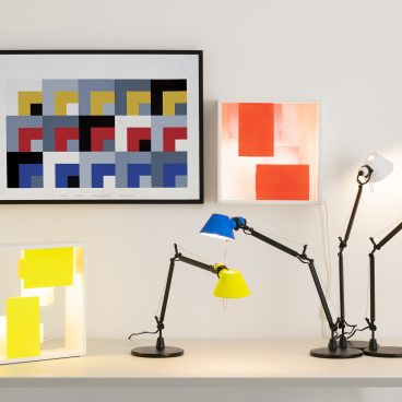 Colorful Tolomeo Micro and Fato bi-color lamps on a table, showcasing Artemide's new design collection against modern art.