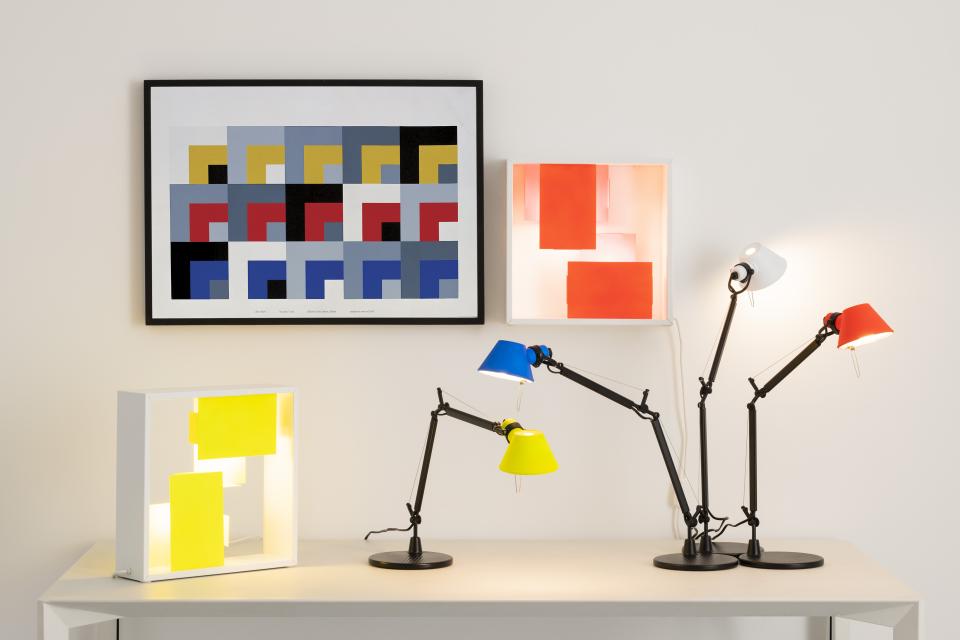 Colorful Tolomeo Micro and Fato bi-color lamps on a table, showcasing Artemide's new design collection against modern art.