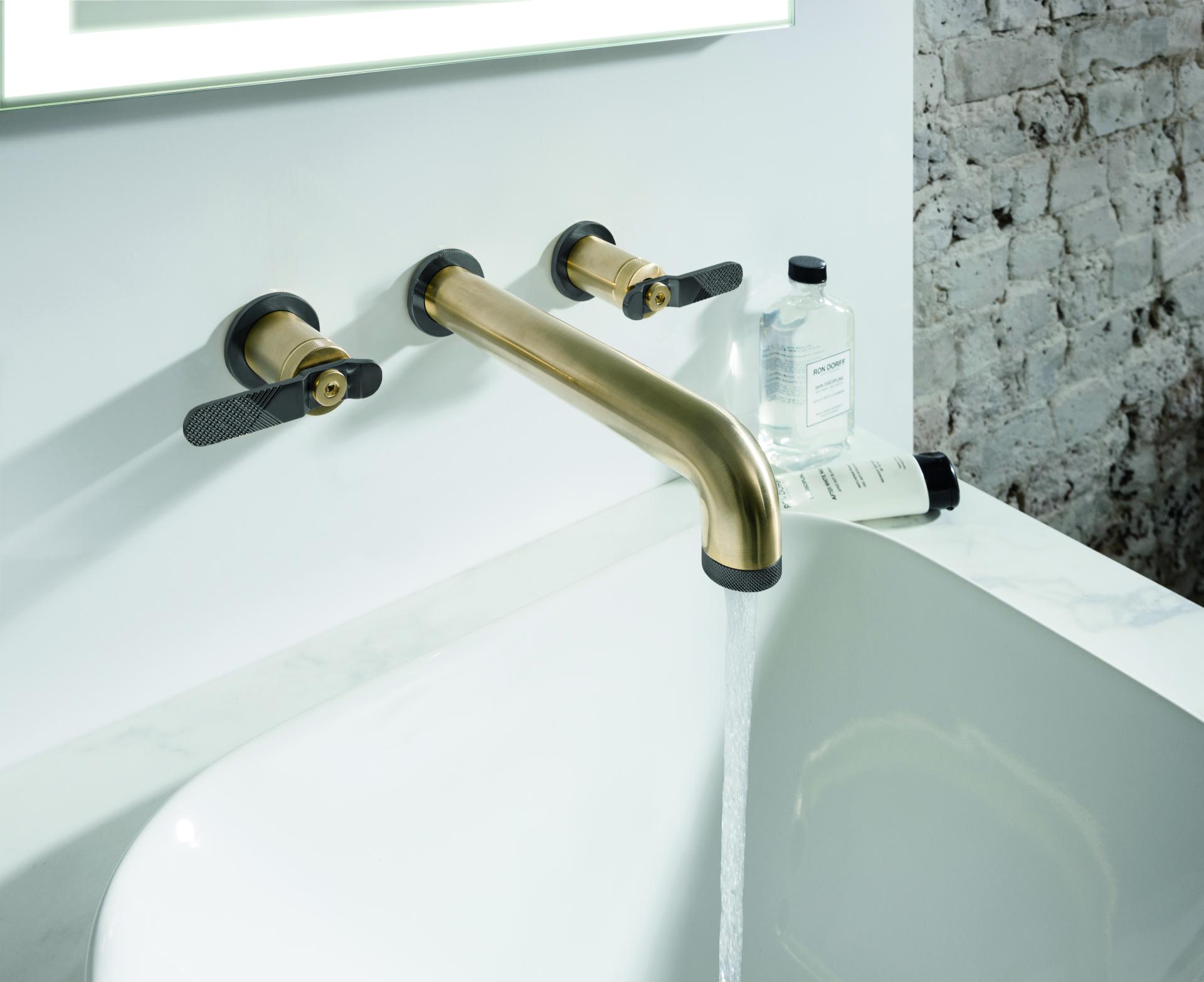 Brass faucet from Crosswater's UNION Mixage collection, featuring industrial design elements and flowing water into a white tub.