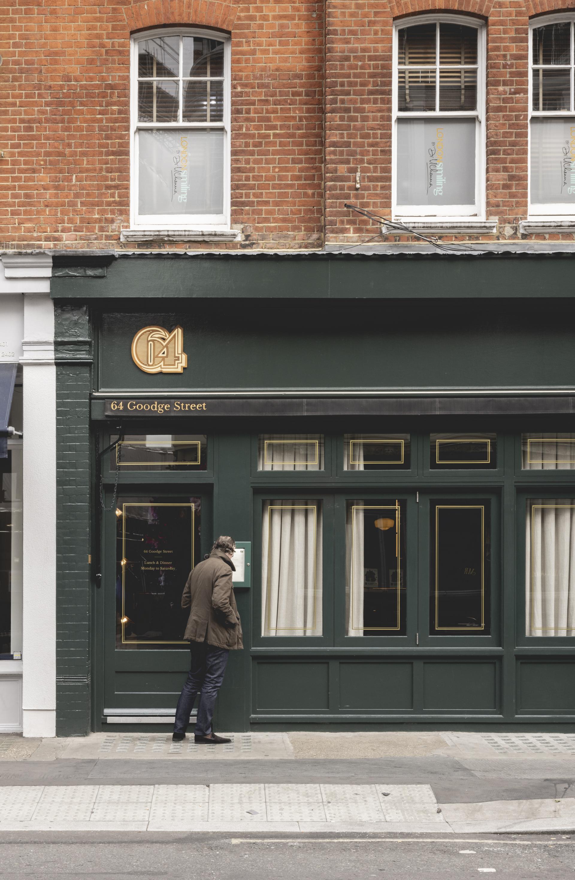 Charming green facade of Fitzrovia restaurant with a man examining the menu outside, blending Parisian and British styles.