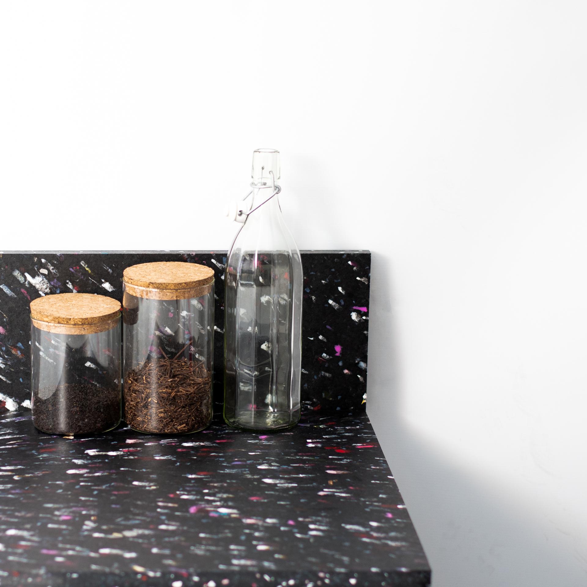 Colorful recycled plastic countertop with glass jars and a bottle, showcasing innovative materials by Smile Plastics.