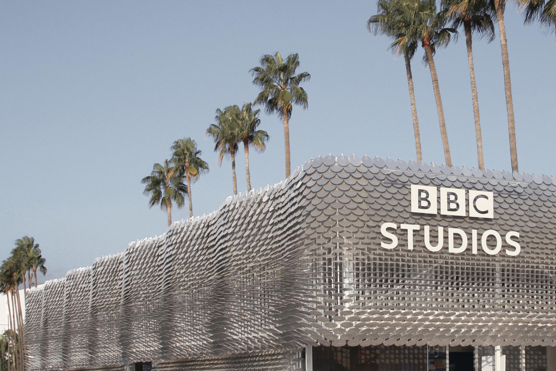 Modern BBC Studios building displays innovative fish-scale architecture, surrounded by palm trees under a clear sky.