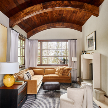 Cozy living room with vaulted wooden ceiling, stylish furniture, and large windows showcasing a serene outdoor view.