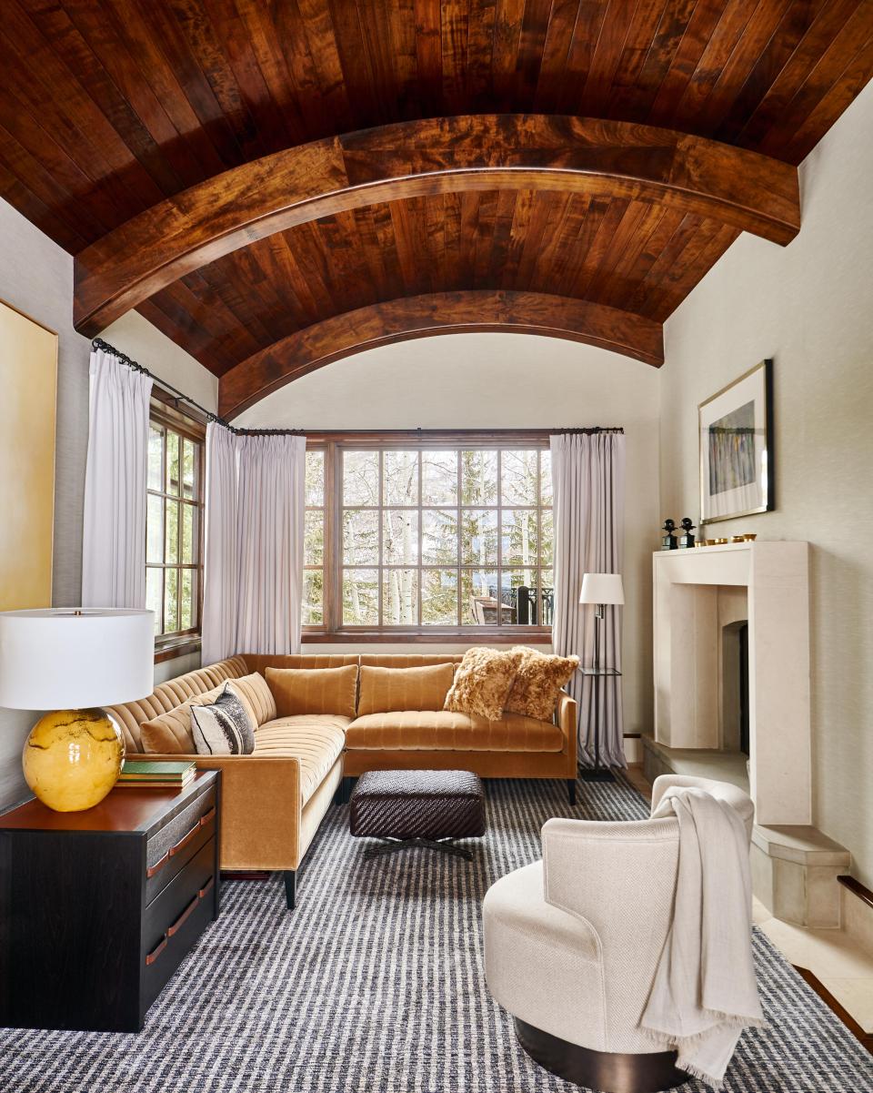 Cozy living room with vaulted wooden ceiling, stylish furniture, and large windows showcasing a serene outdoor view.