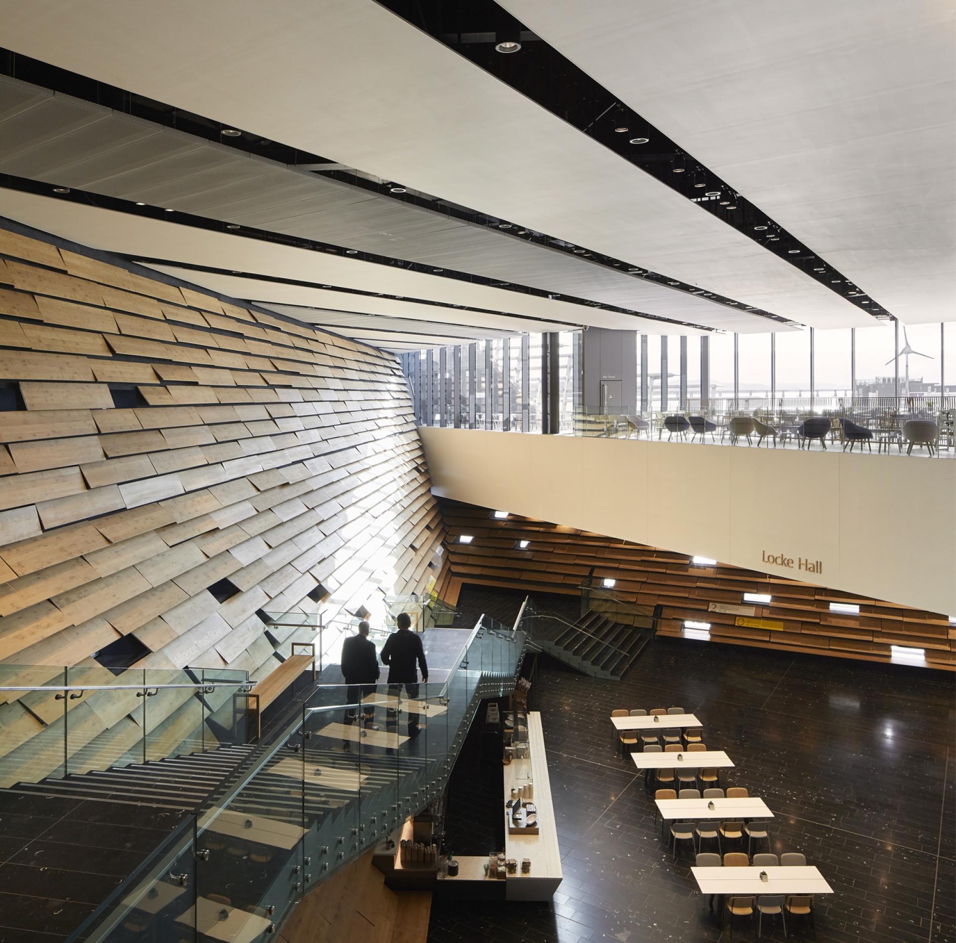 Light-filled interior of V&A Dundee showcasing wooden walls, central staircase, and dining area designed by Kengo Kuma.