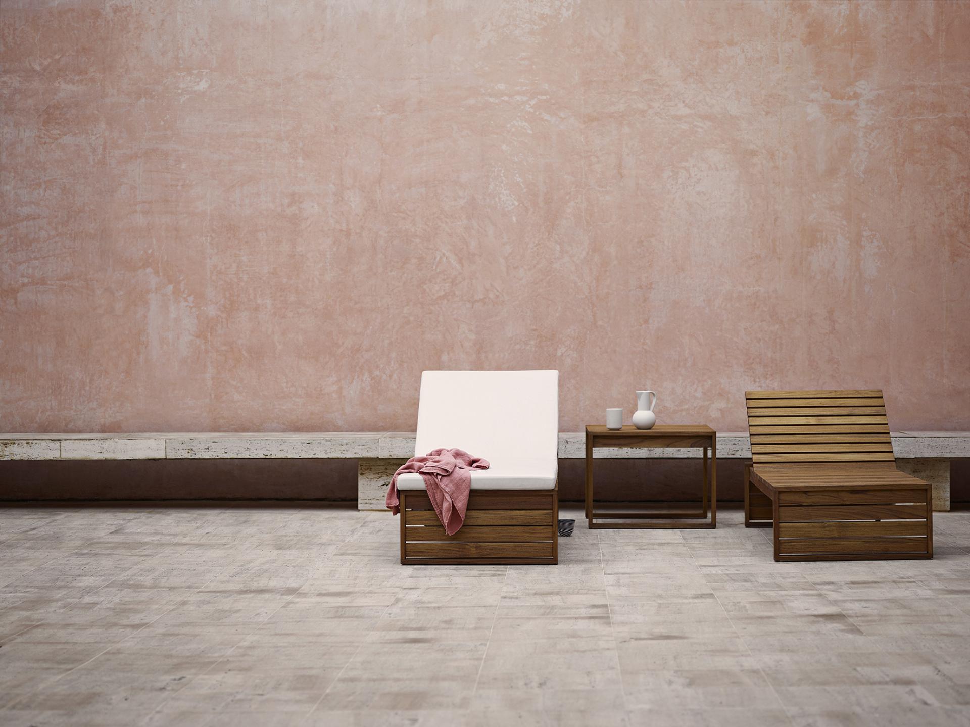 Bodil Kjær's architectural furniture in a serene setting, featuring wooden lounge chairs and a minimalist side table.