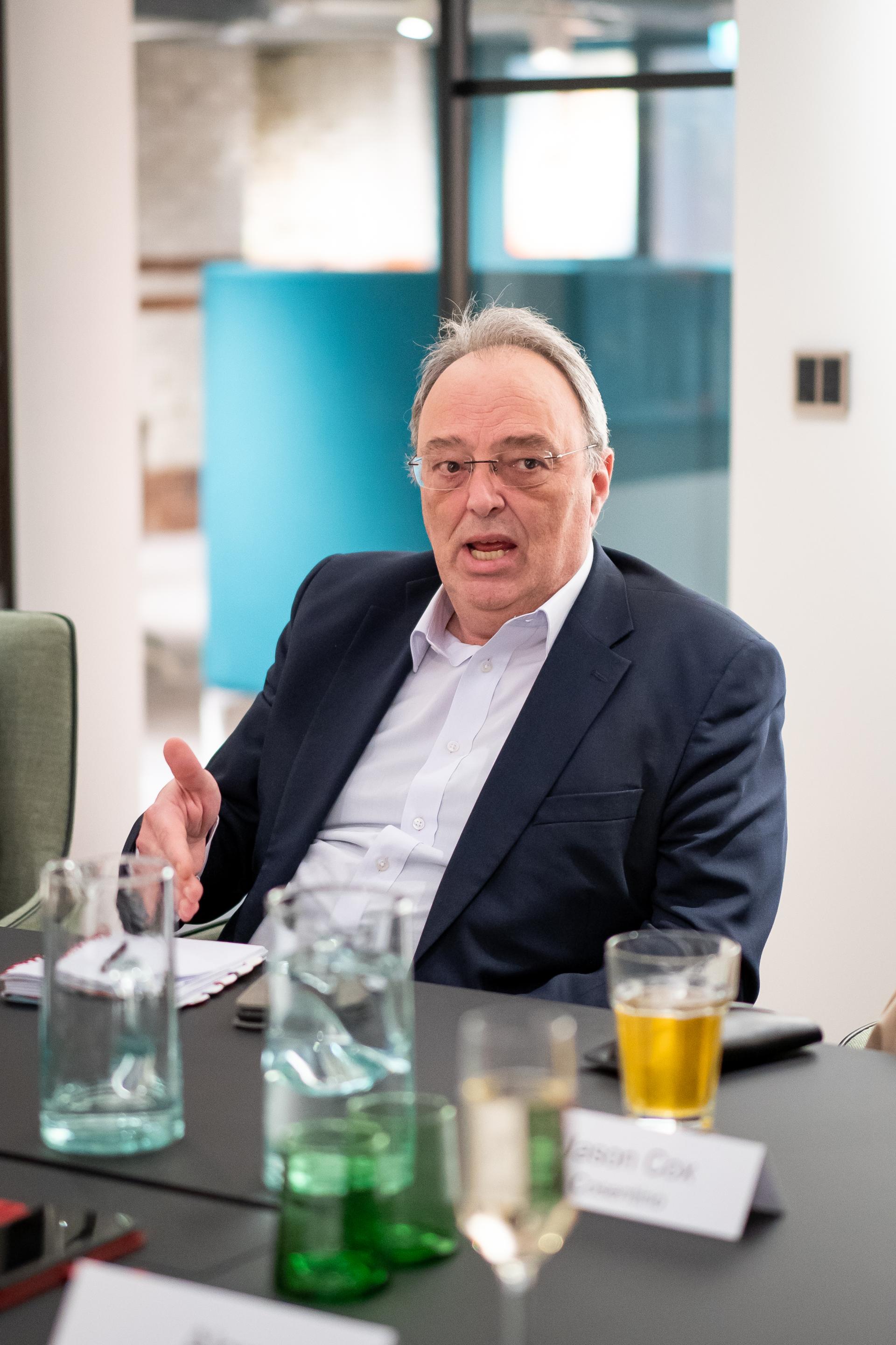 Business leader discussing sustainability strategies at a roundtable meeting with drinks and notebooks present.