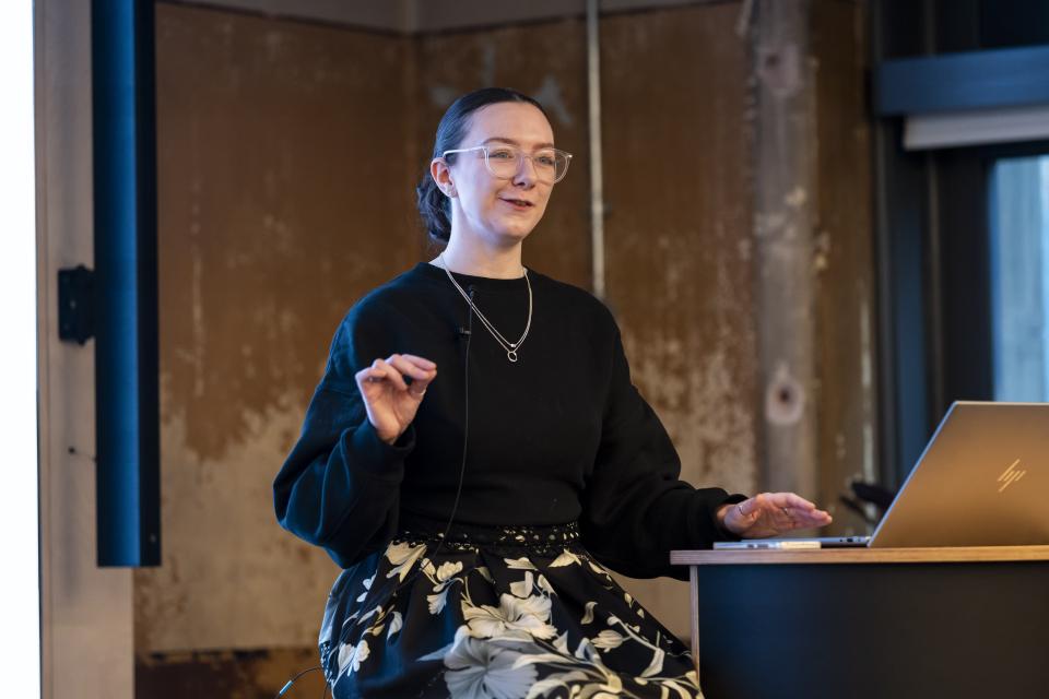 Senior architect Stephanie Kyle speaking at a conference about neurodiversity and inclusive design, gesturing while seated at a desk.
