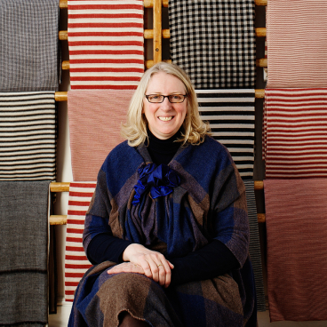 Polly Leonard, founder of Selvedge magazine, poses in front of colorful textiles, showcasing raw design talent in the industry.