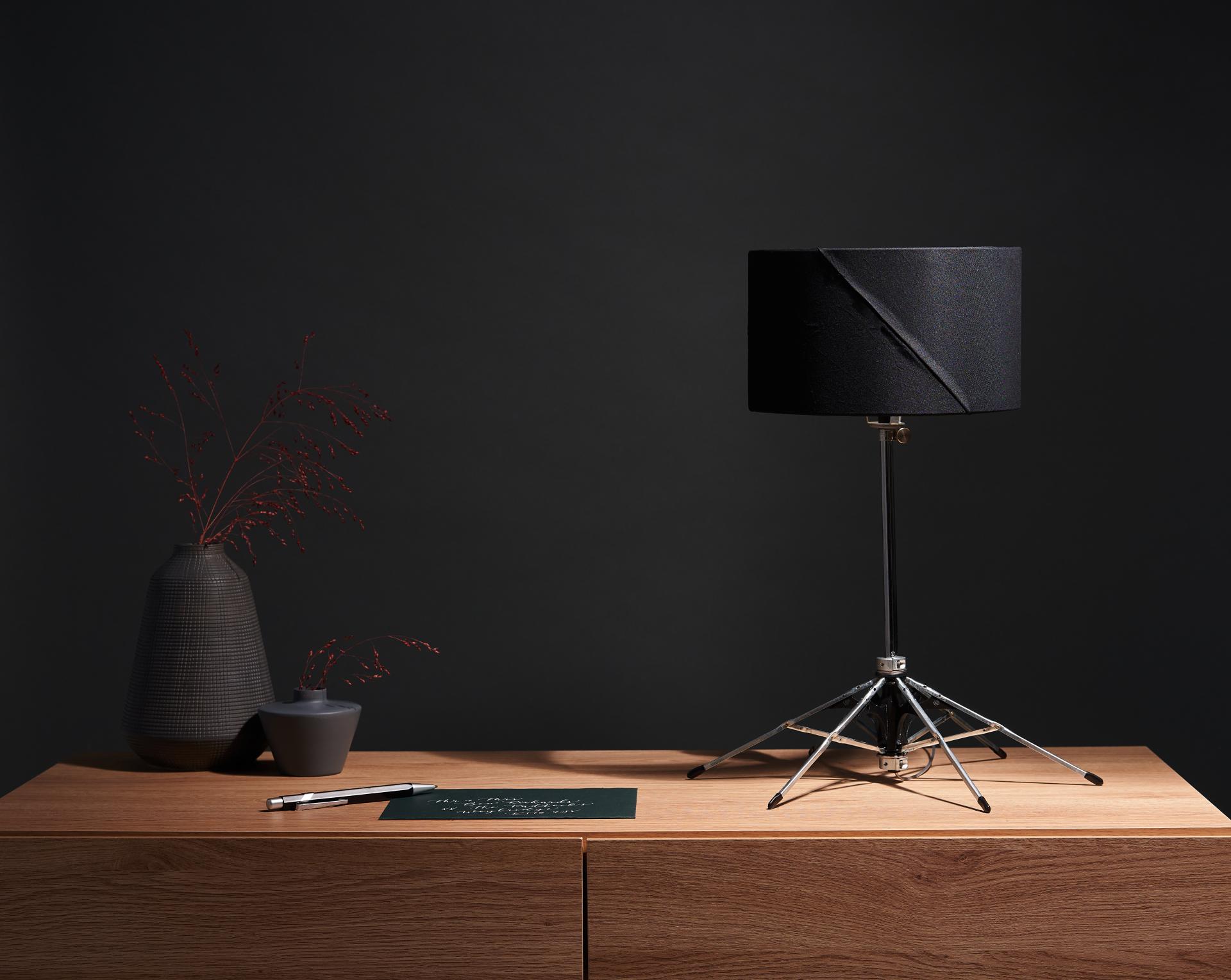 Upcycled lamp made from discarded umbrellas, featuring a black shade and tripod base, displayed on a wooden surface.