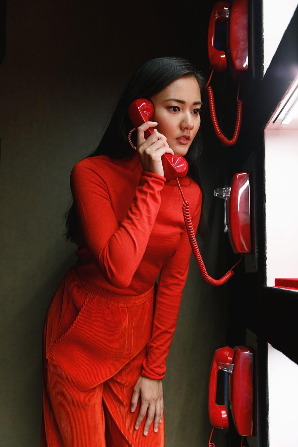 A woman in a red outfit interacts with a vintage red telephone in the colorful Color Factory exhibit.