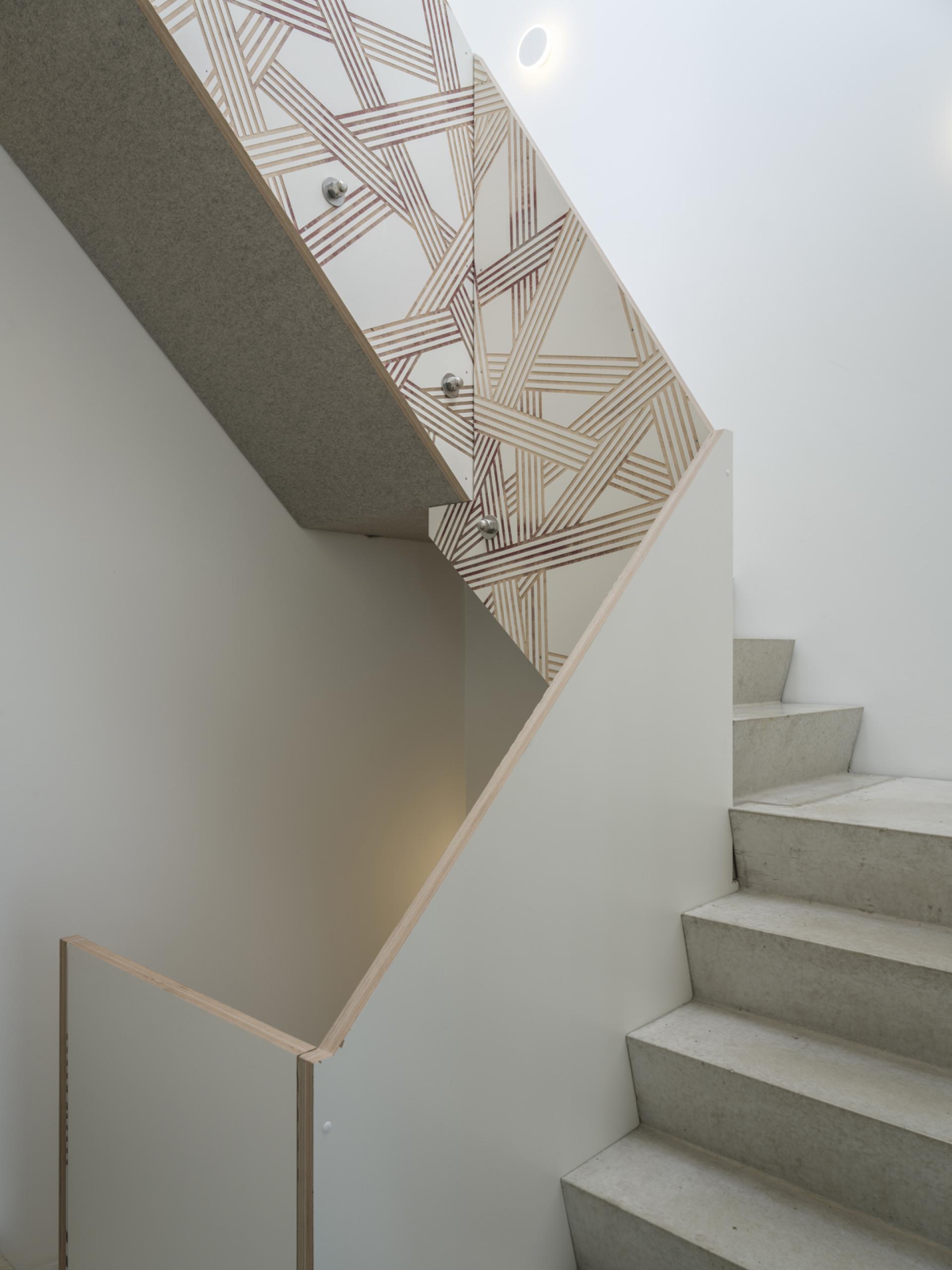 Modern staircase in thonik’s new Amsterdam studio, featuring unique patterned wall design and concrete steps.