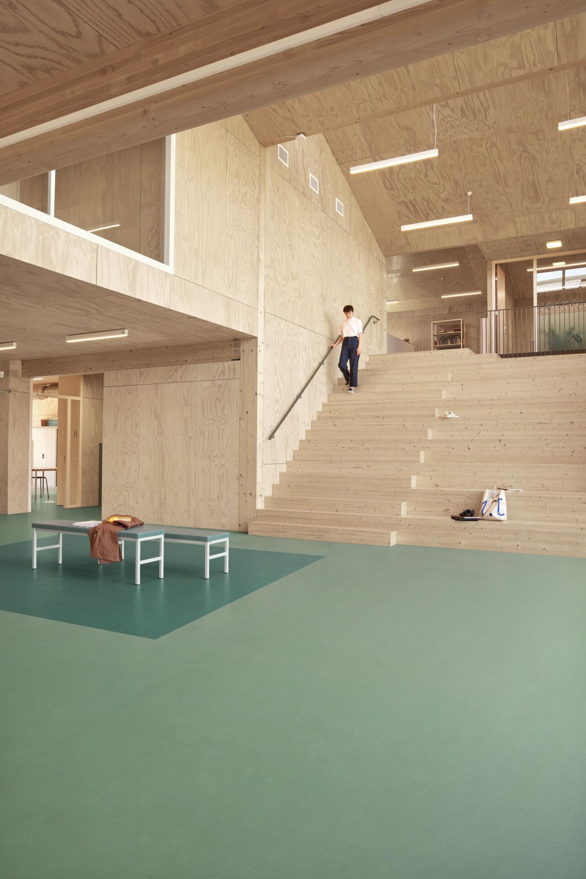 Spacious interior featuring Forbo's Marmoleum Solids flooring, with modern wood accents and a person ascending the staircase.