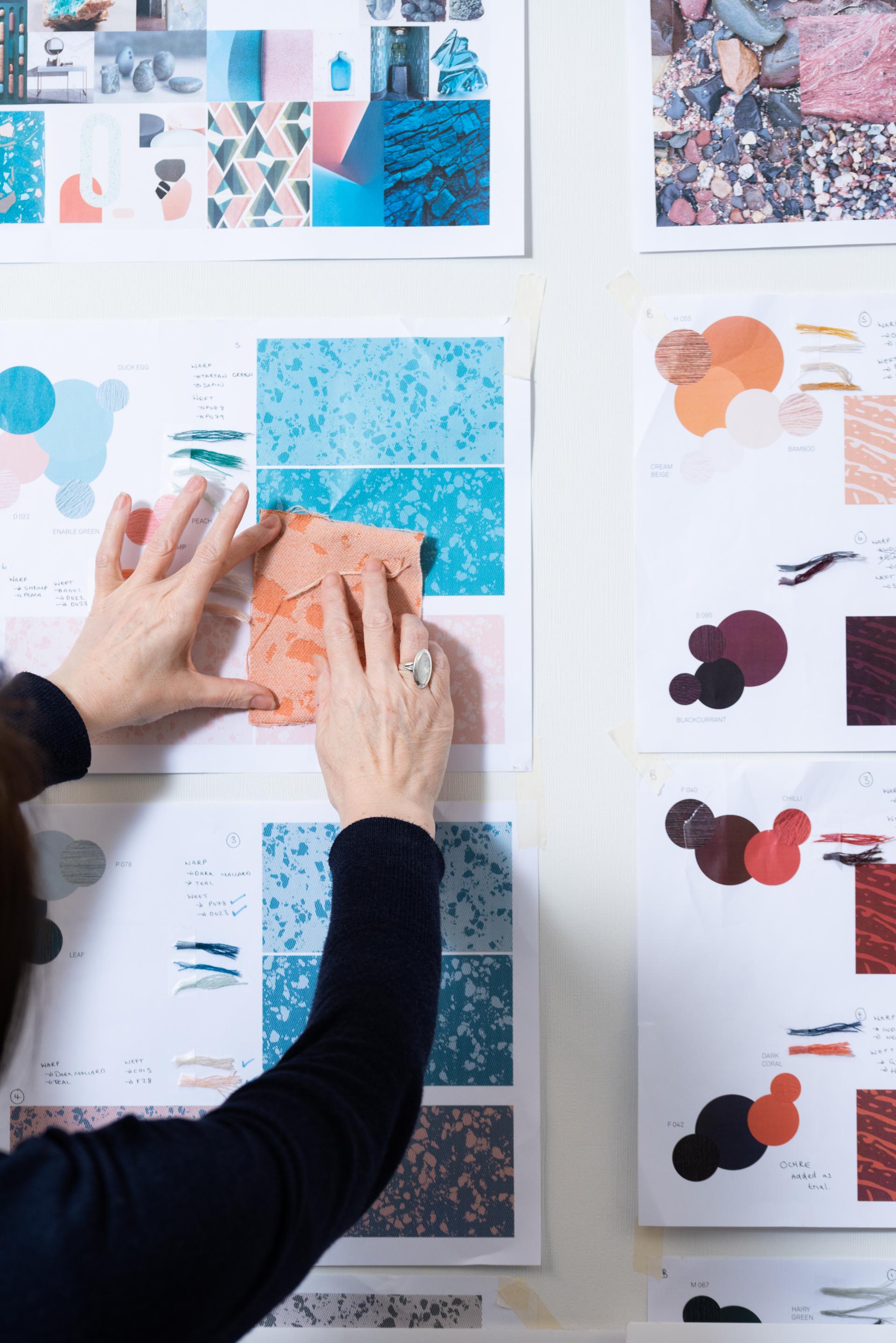 A designer arranges color samples and patterns for David Irwin x Bute Fabrics collaboration, showcasing textile creativity.