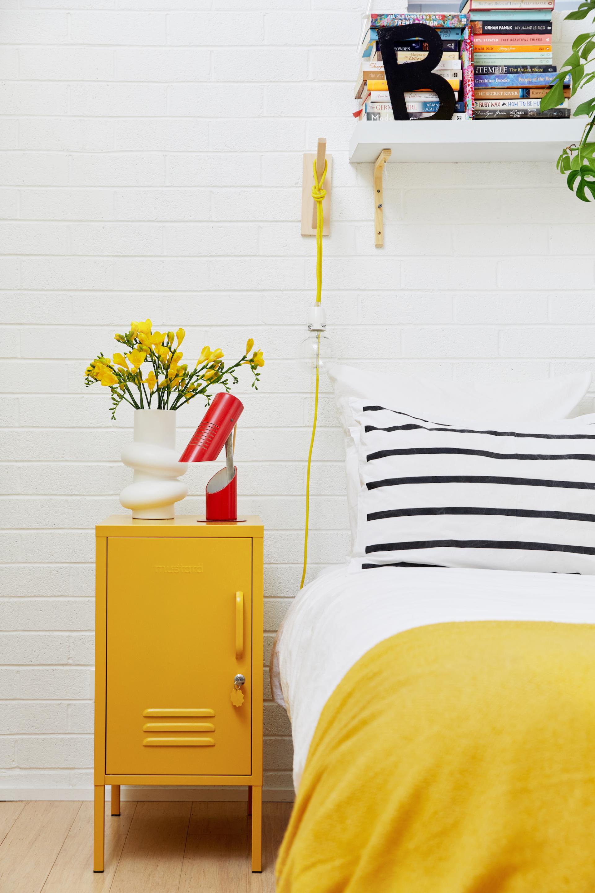 Bright yellow nightstand with flowers, unique lamp, and striped bedding, showcasing playful and practical design in interior decor.