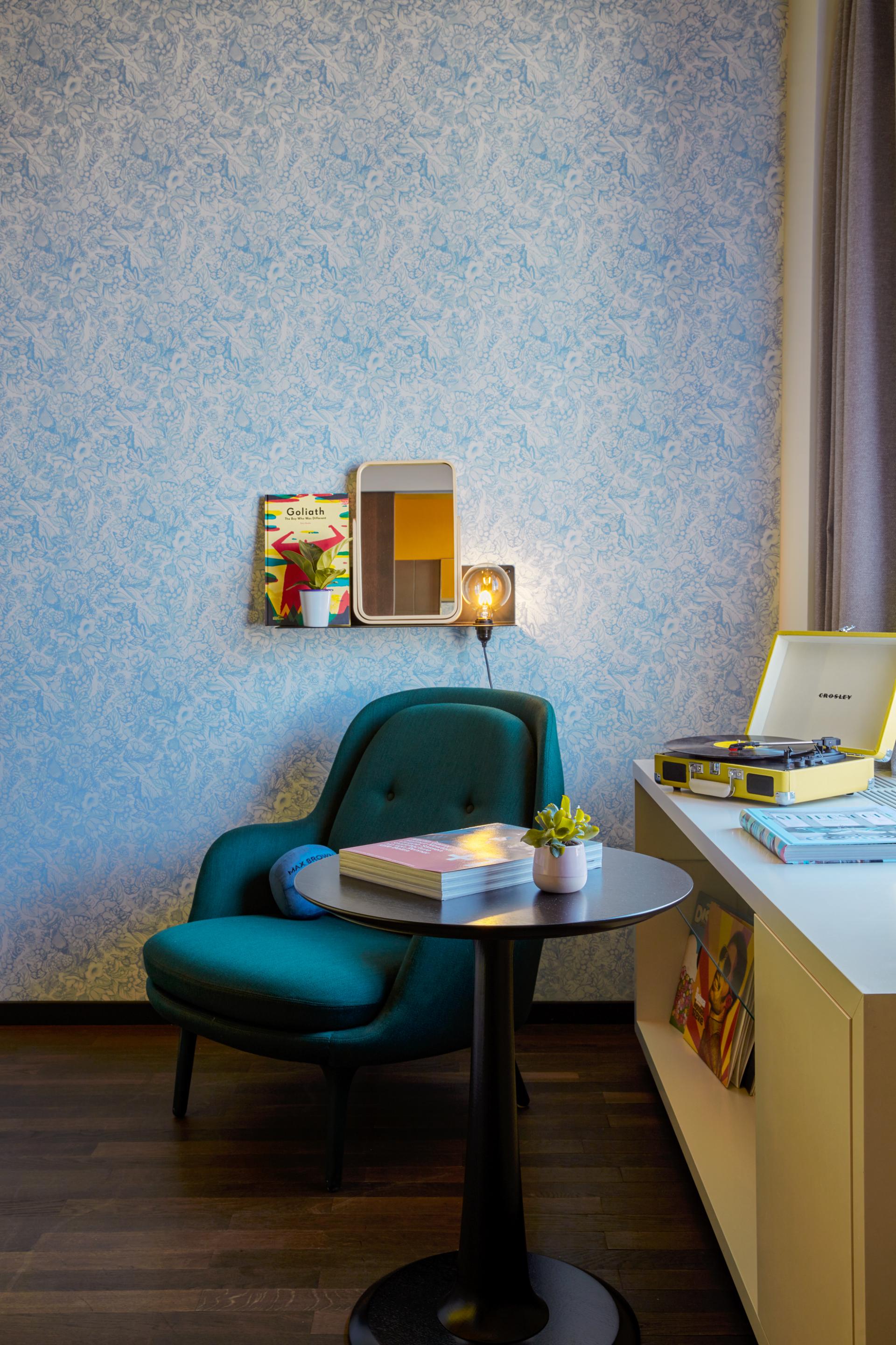 Cozy corner of a stylish hotel room featuring a green chair, decorative wall, and vintage record player in Vienna.