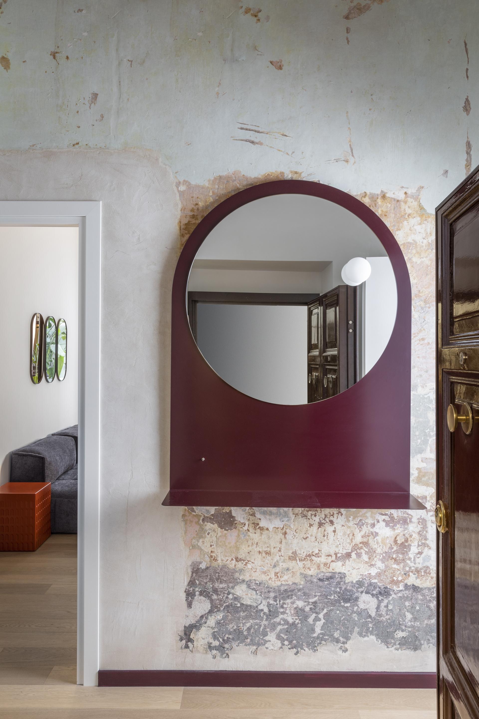 Modern apartment entryway in Trastevere, featuring a round mirror and textured wall, reflecting contemporary design.