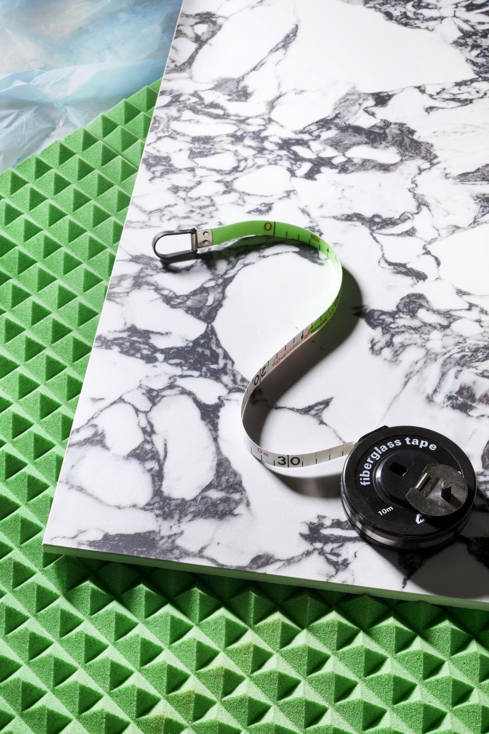Materials and tools for interior design project, showcasing green acoustic foam, marble sample, and measuring tape for restaurant design.