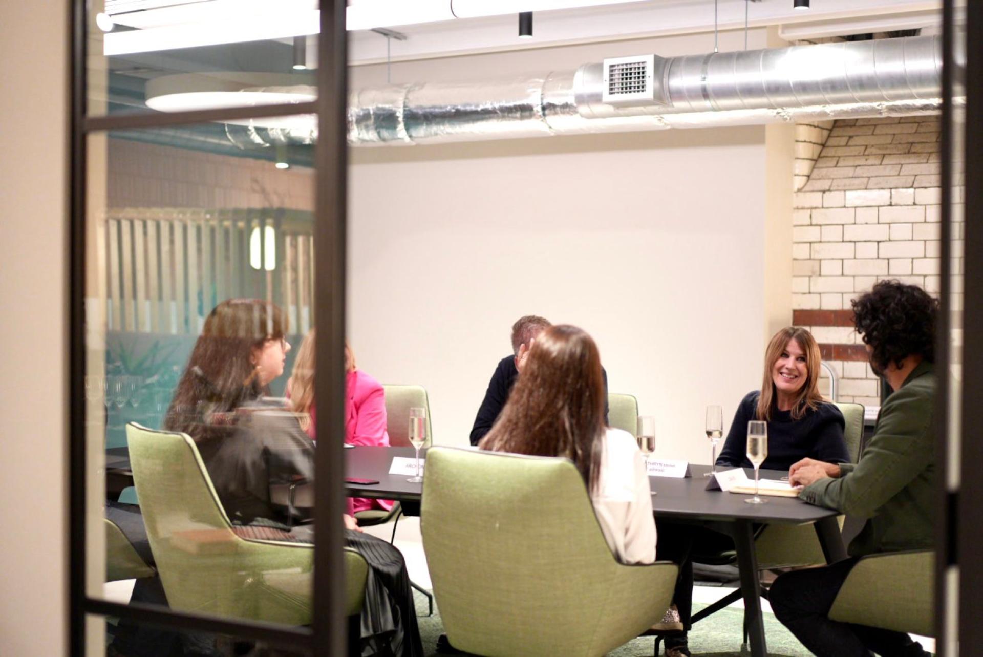 Group of professionals engaged in discussion around a modern conference table in a contemporary workplace setting.