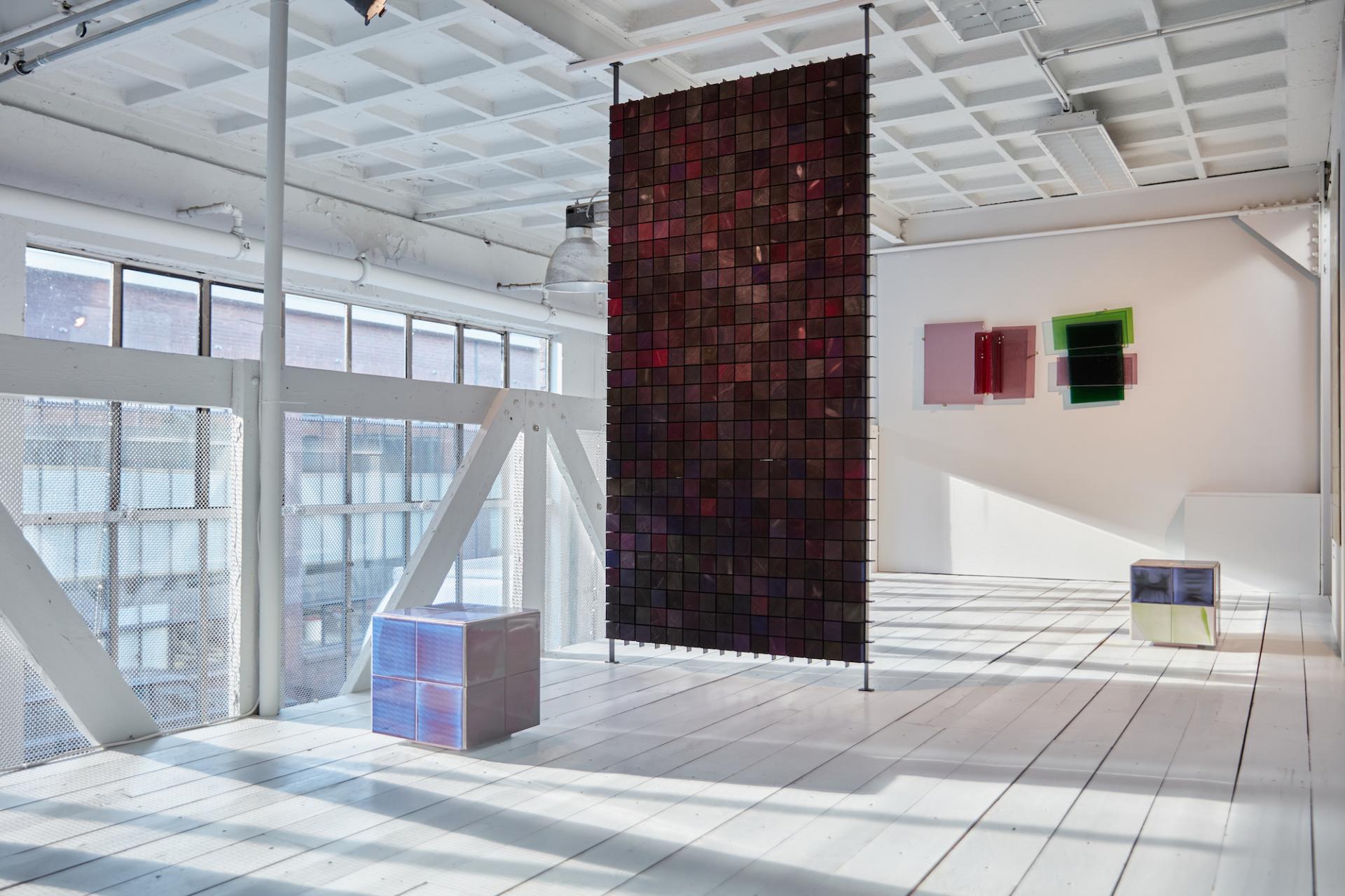 Colorful translucent cubes and a vibrant wall hanging create a striking visual in a bright design exhibition space.