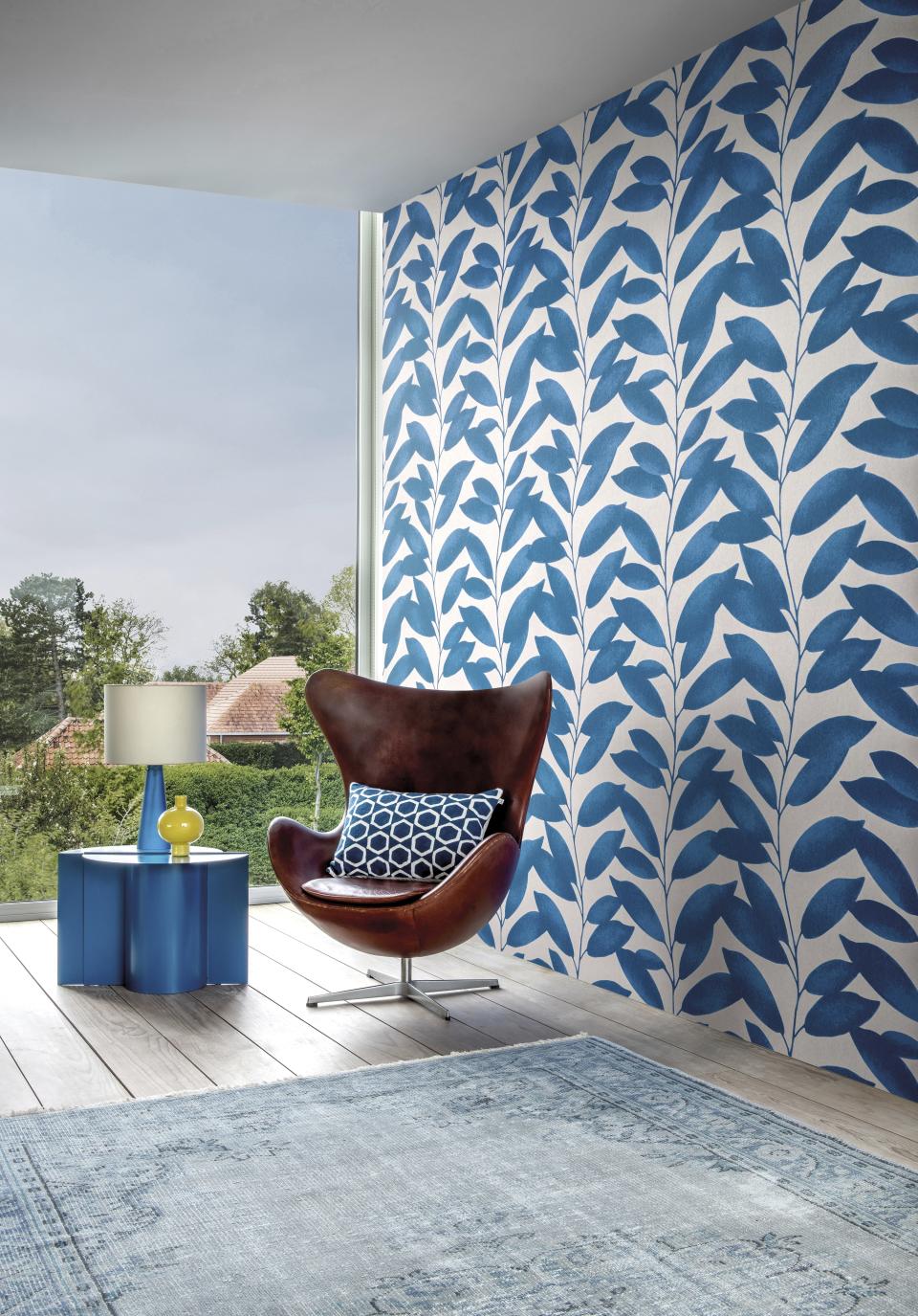 Stylish room featuring Omexo's blue leaf-patterned wallcovering, a modern chair, and contemporary decor elements.