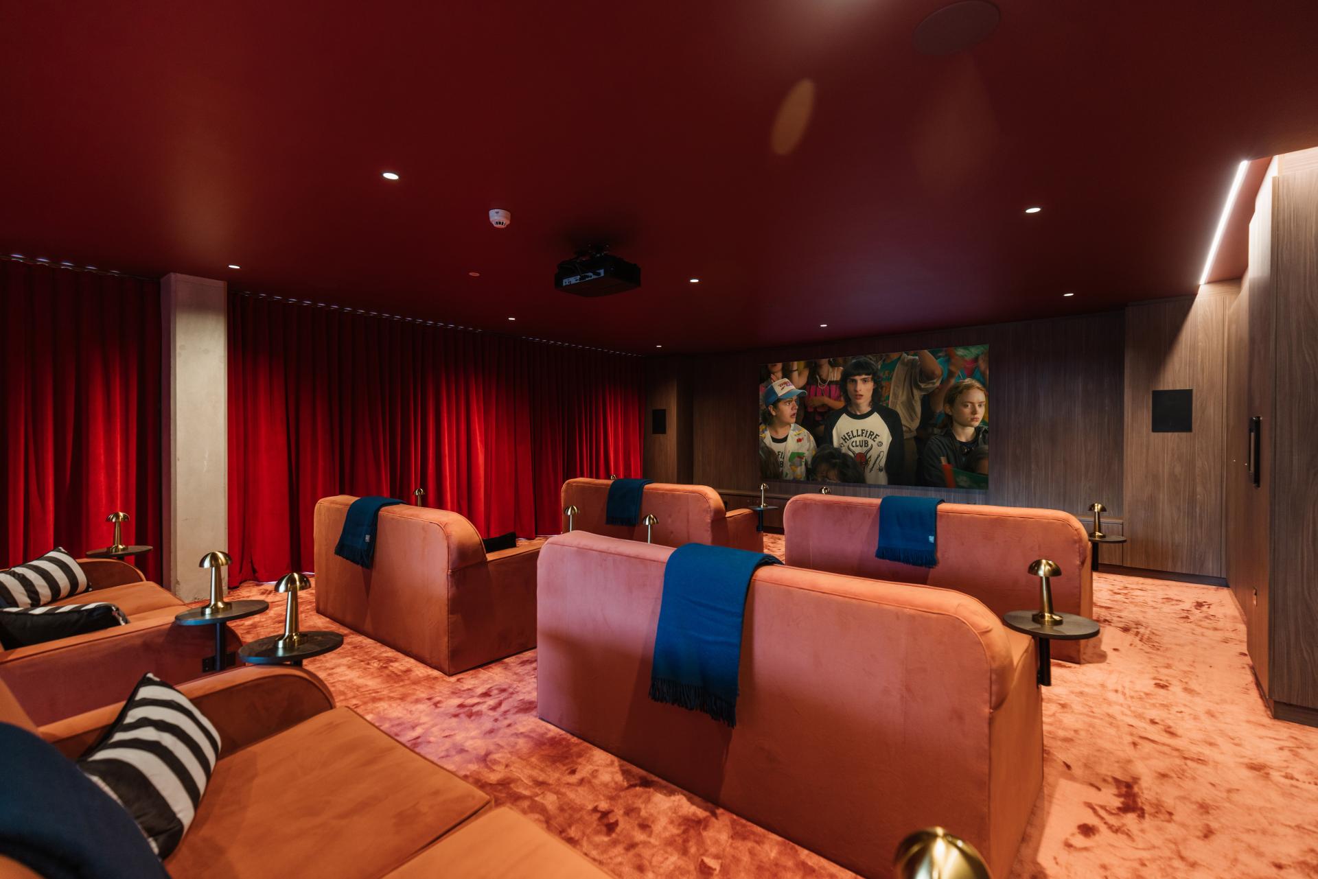 Stylish private cinema room featuring plush seating, red velvet curtains, and a large screen for entertainment.