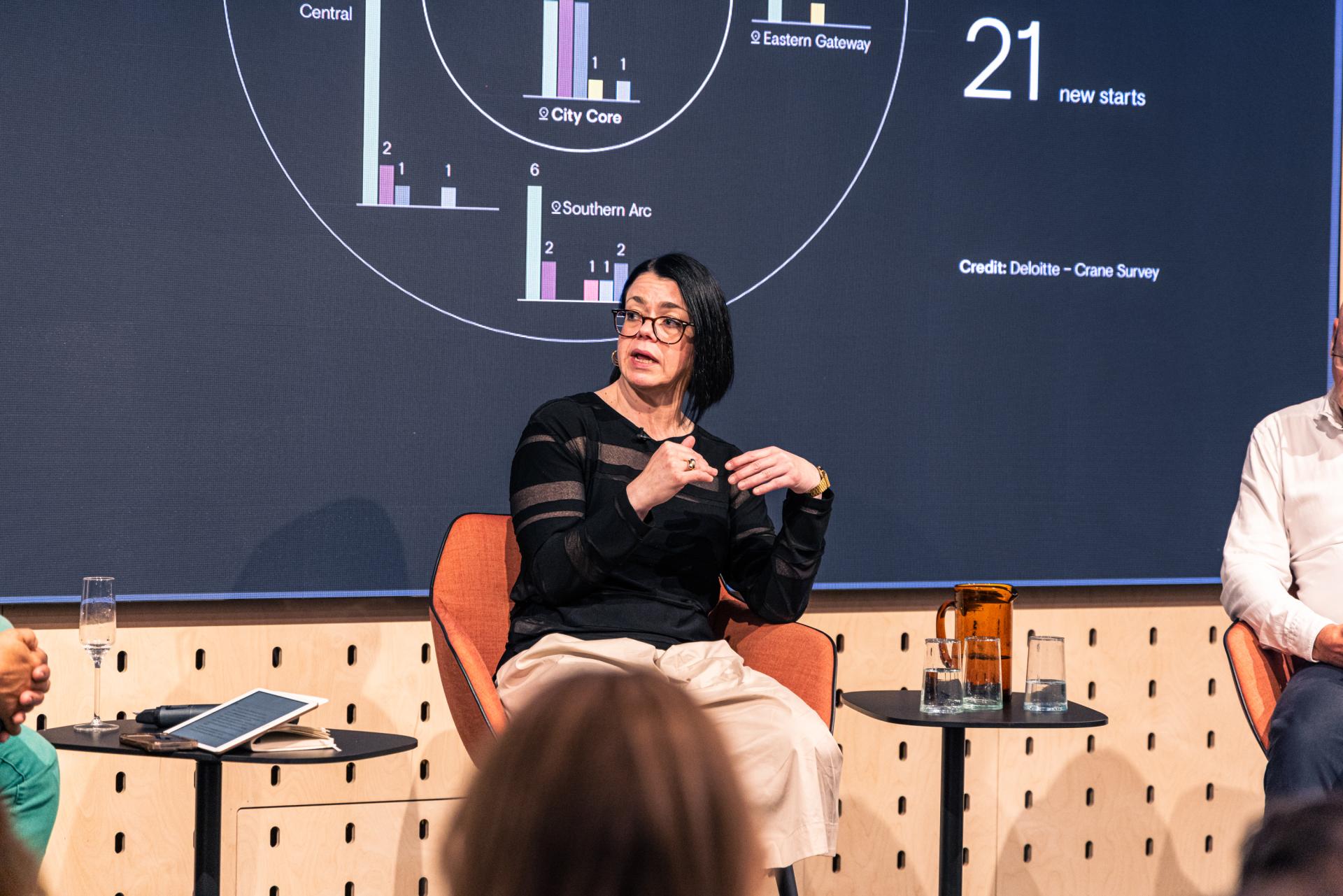 Female panelist discusses Manchester property growth, with graphs displayed on a screen during a seminar.