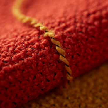 Textured red fabric detail showcasing sustainable British manufacturing, featuring woven fibers and contrasting yellow stitching.