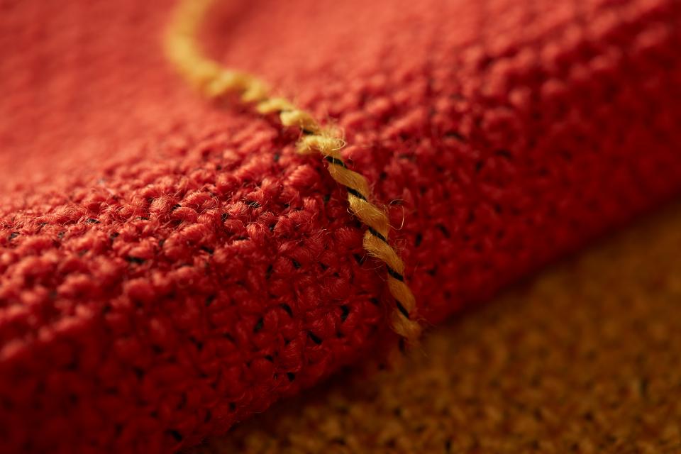 Textured red fabric detail showcasing sustainable British manufacturing, featuring woven fibers and contrasting yellow stitching.