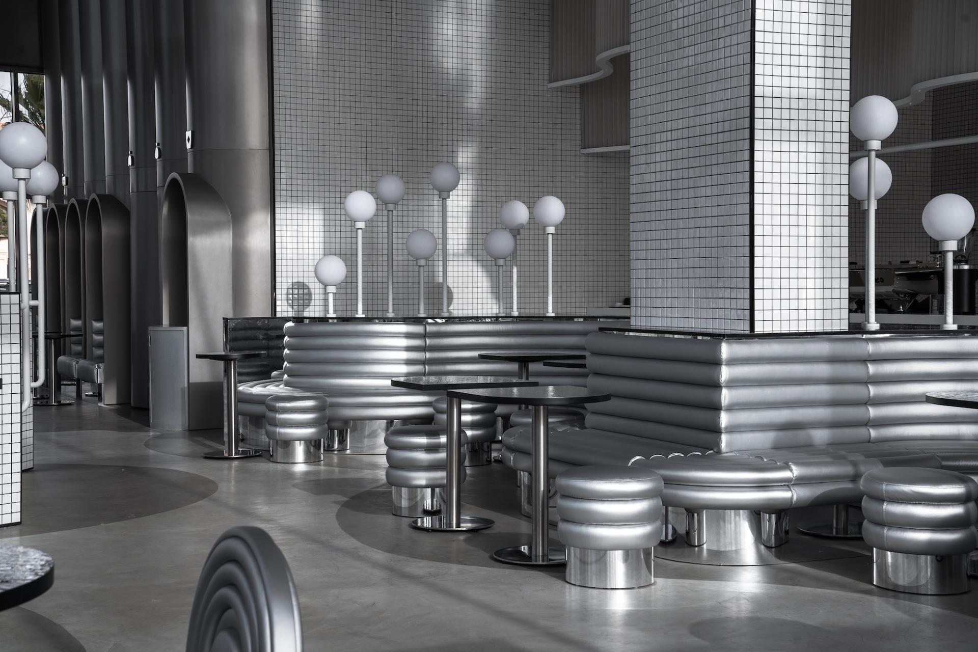 Contemporary interior design of MO bakehouse and espresso bar featuring sleek silver seating and glowing round lamps.