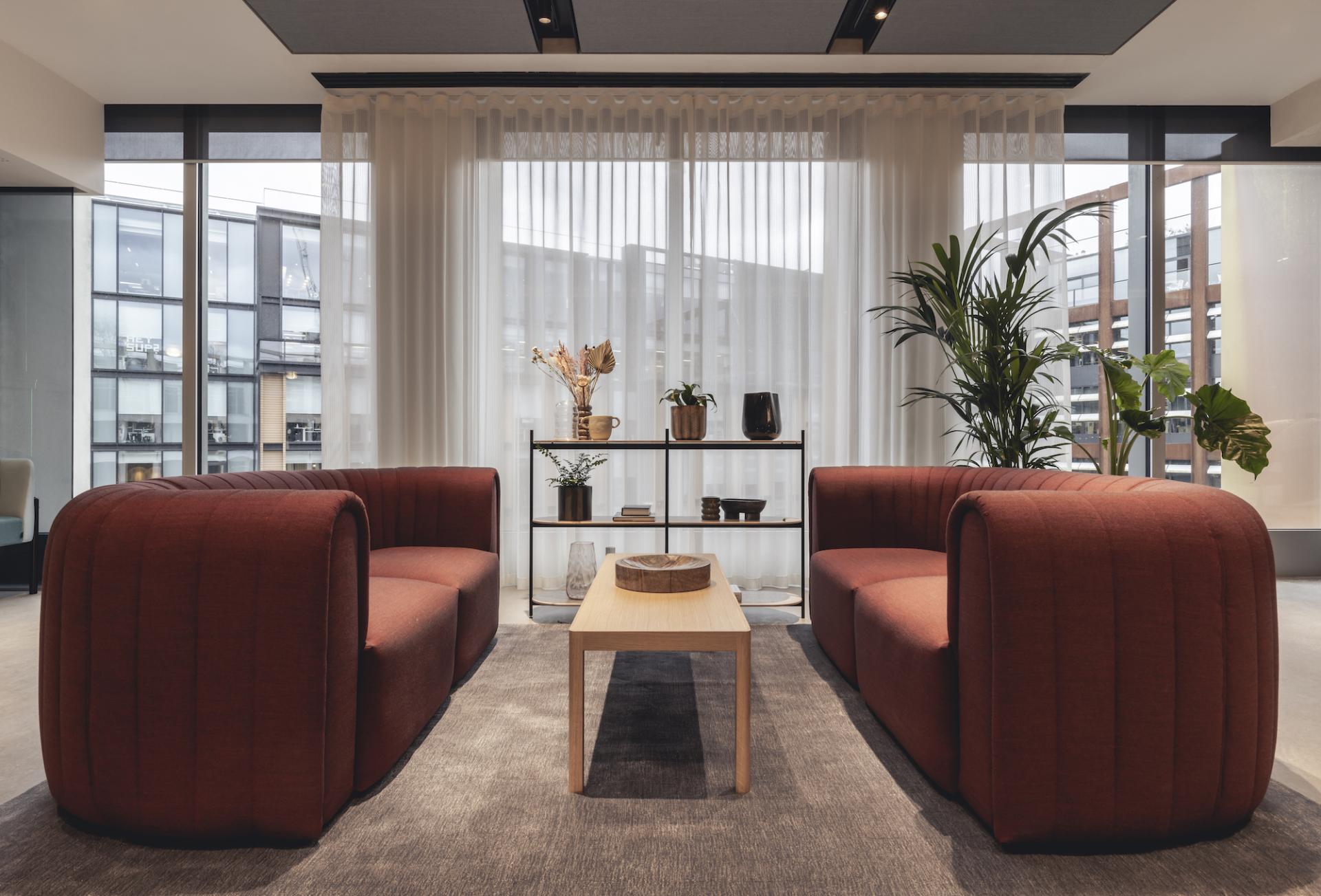Stylish seating area featuring contemporary red sofas, a wooden table, and decorative plants in a modern workspace.