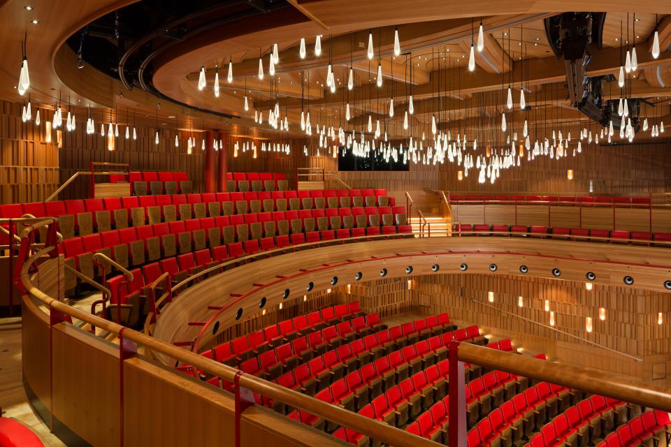 Contemporary theater interior featuring red seating, wooden elements, and unique hanging light fixtures, highlighting innovative design.