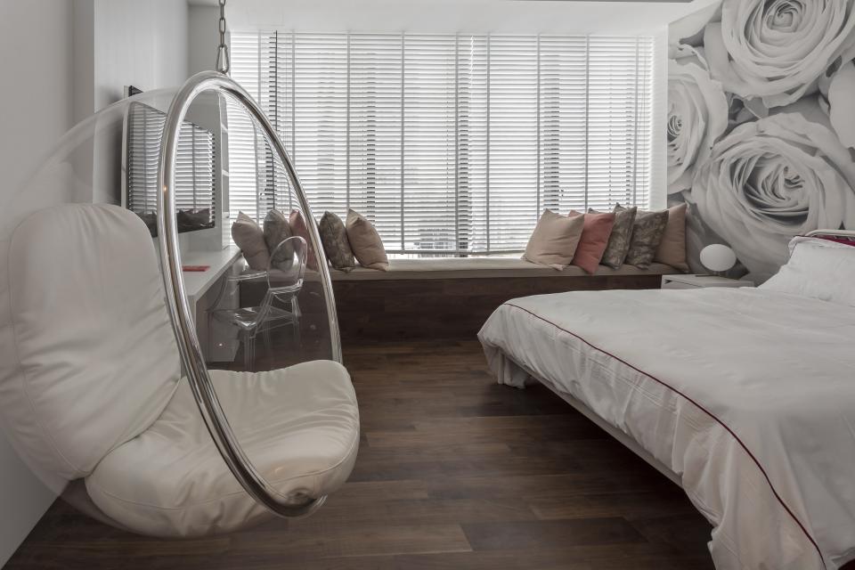 Modern bedroom featuring a transparent hanging chair, elegant decor, and a vibrant rose mural, showcasing Elliot James' award-winning design.