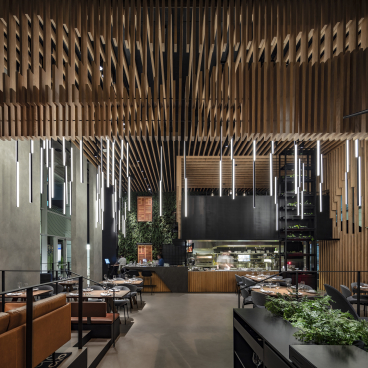 Double-height restaurant interior featuring suspended wooden beams and modern lighting, designed by Kimmel Eshkolot Architects.