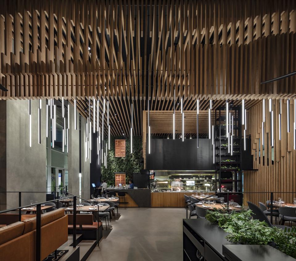 Double-height restaurant interior featuring suspended wooden beams and modern lighting, designed by Kimmel Eshkolot Architects.