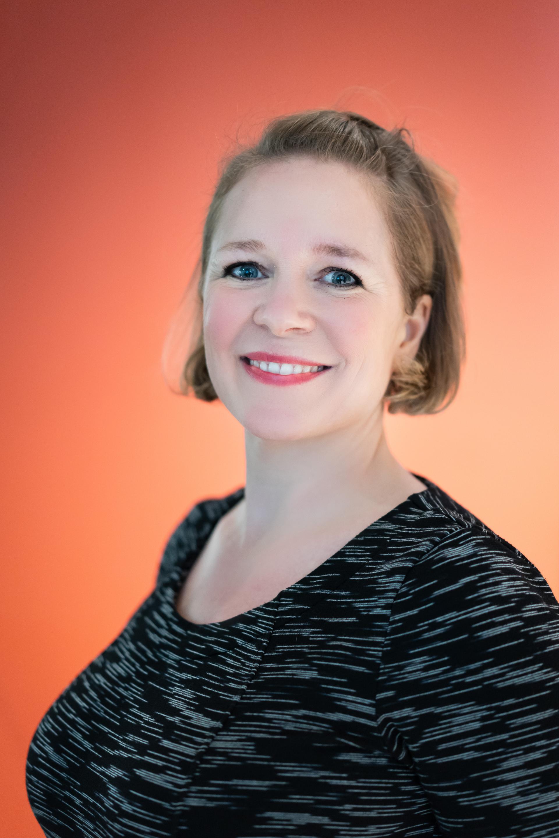 Professional woman smiling against a vibrant orange backdrop, representing the future of workplace flexibility and collaboration.