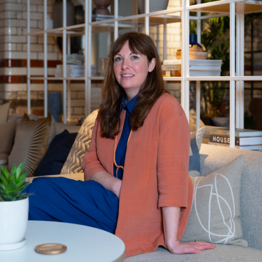 Laura Perryman, a CMF designer, seated on a stylish sofa with decorative cushions, discussing color theory and nature's imperfections.