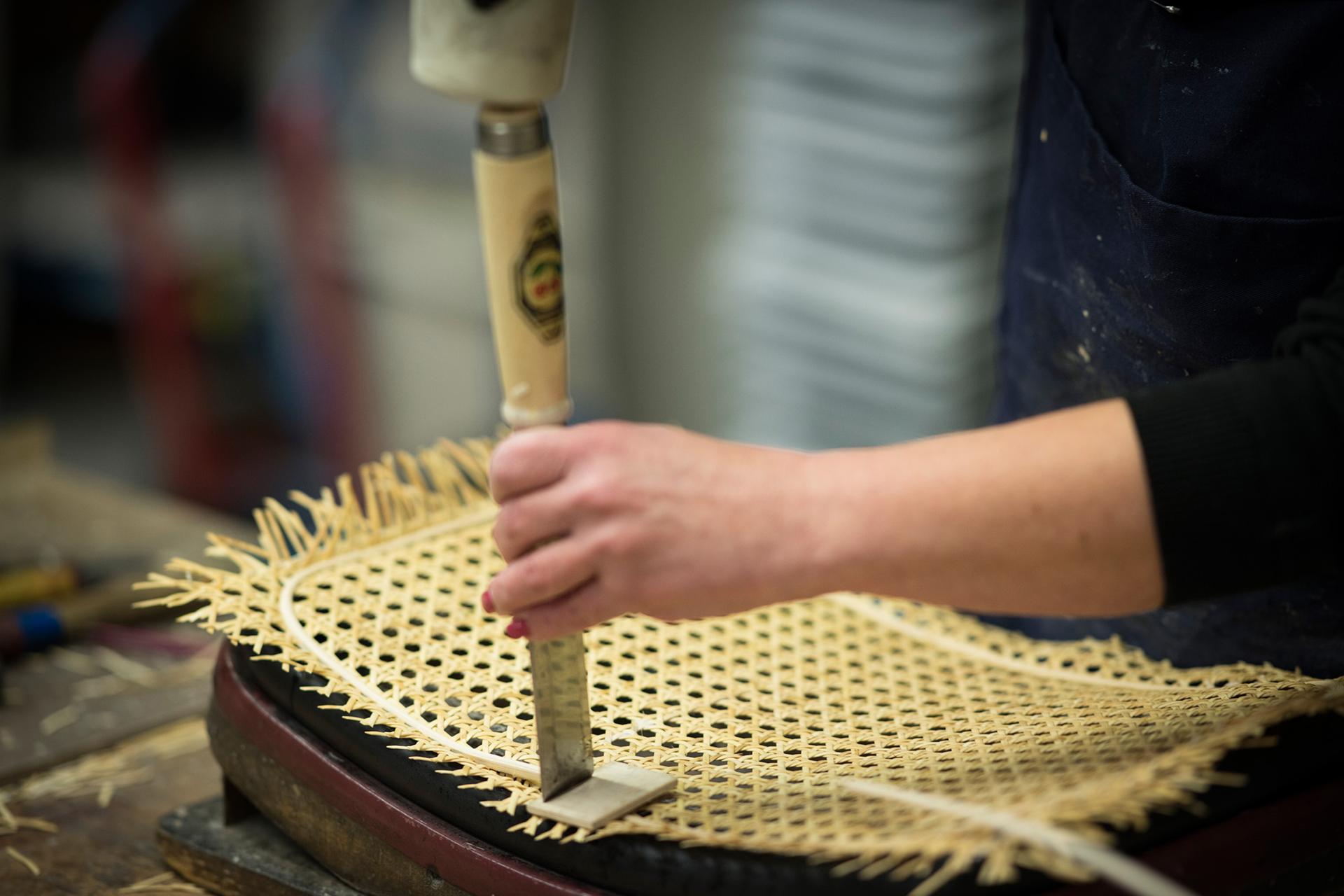 Craftsman meticulously weaving wicker material into a chair at Thonet's production facility in Germany.