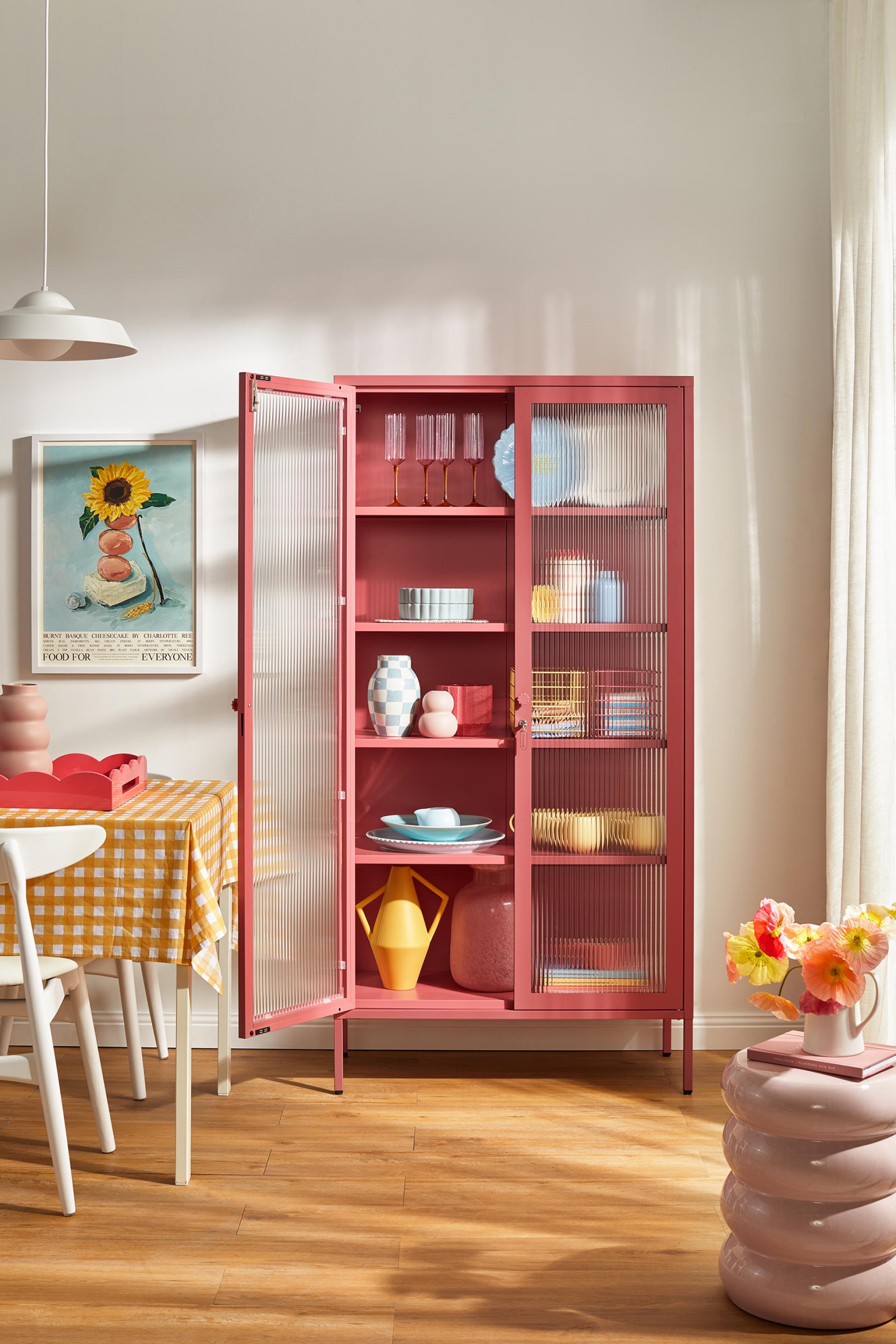 Vibrant pink cabinet showcasing colorful dishware and decor, highlighting Mustard Made's new Glass Collection for playful interiors.
