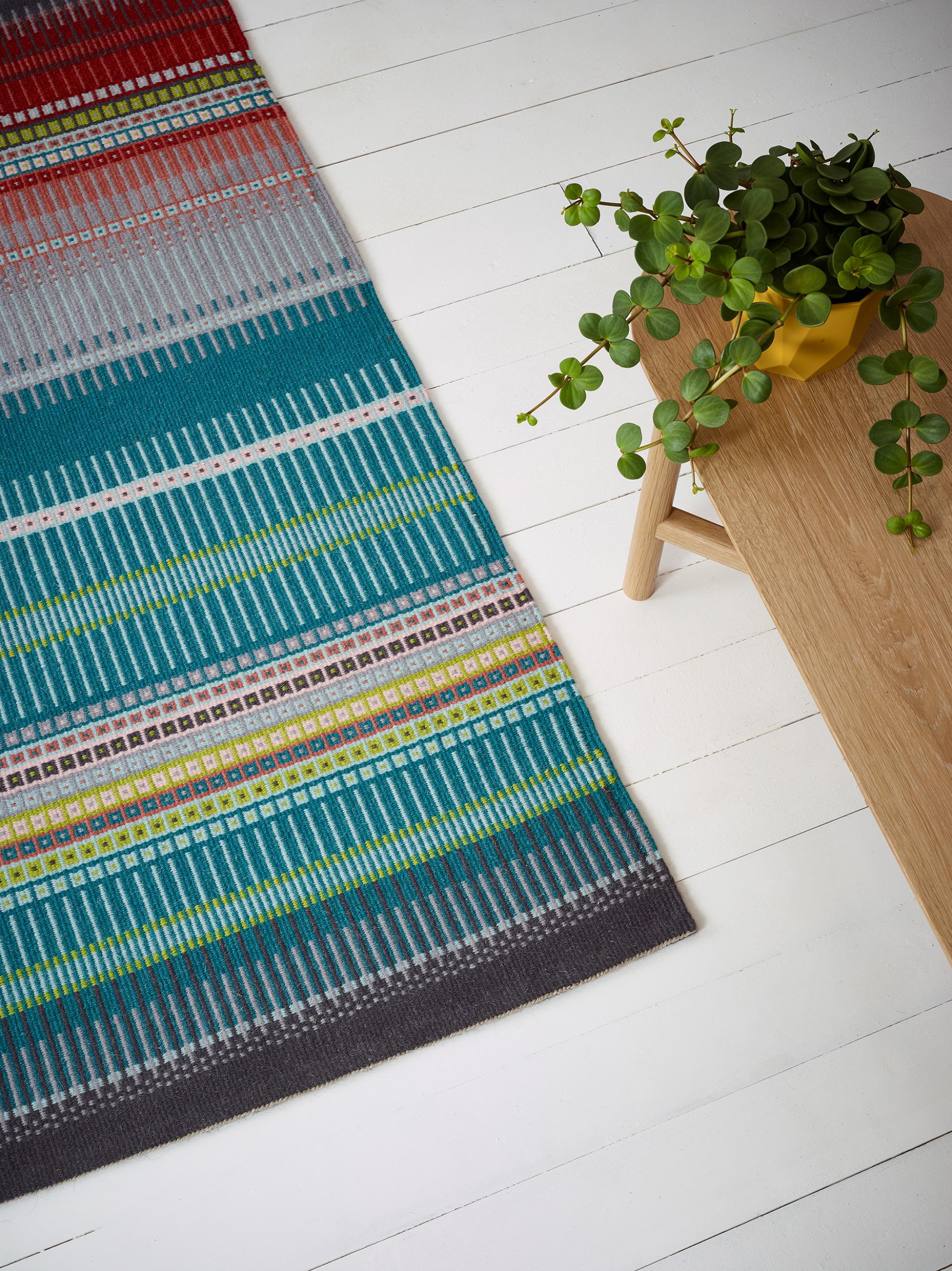 Colorful woven rug on a white wooden floor, accompanied by a wooden table and green potted plant, showcasing Bristol's creative craft.