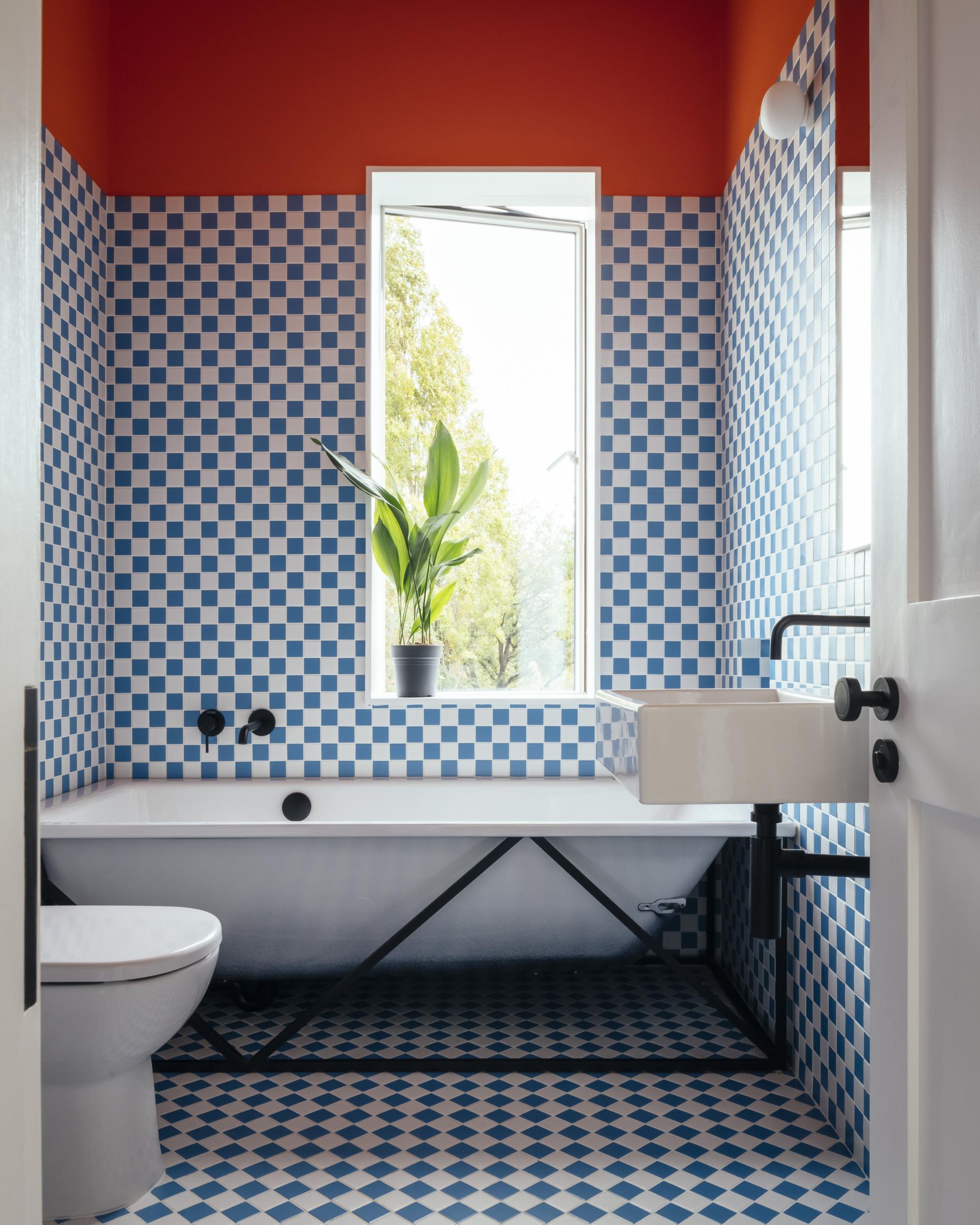 Colorful bathroom featuring blue and white checkered tiles, a freestanding tub, and vibrant orange walls in a renovated Edwardian home.