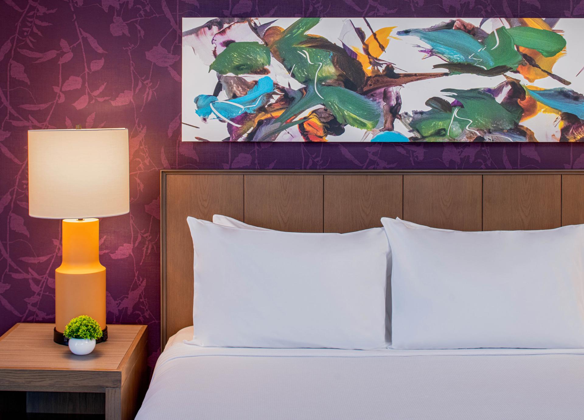 Vibrant hotel bedroom featuring a colorful abstract art piece, plush white bedding, and a stylish lamp in Hyatt House, Tampa.