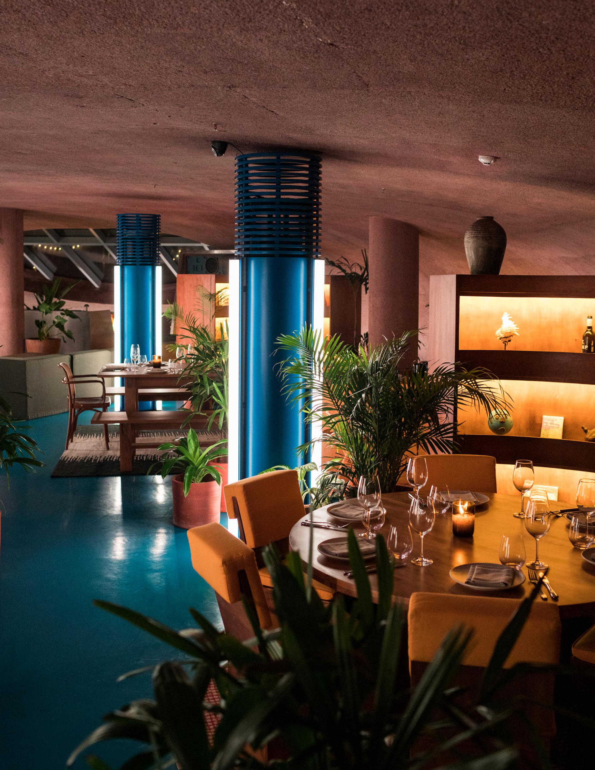 Sleek dining area at Desa Potato Head's Dome, featuring vibrant blue accents, earthy tones, and lush greenery.