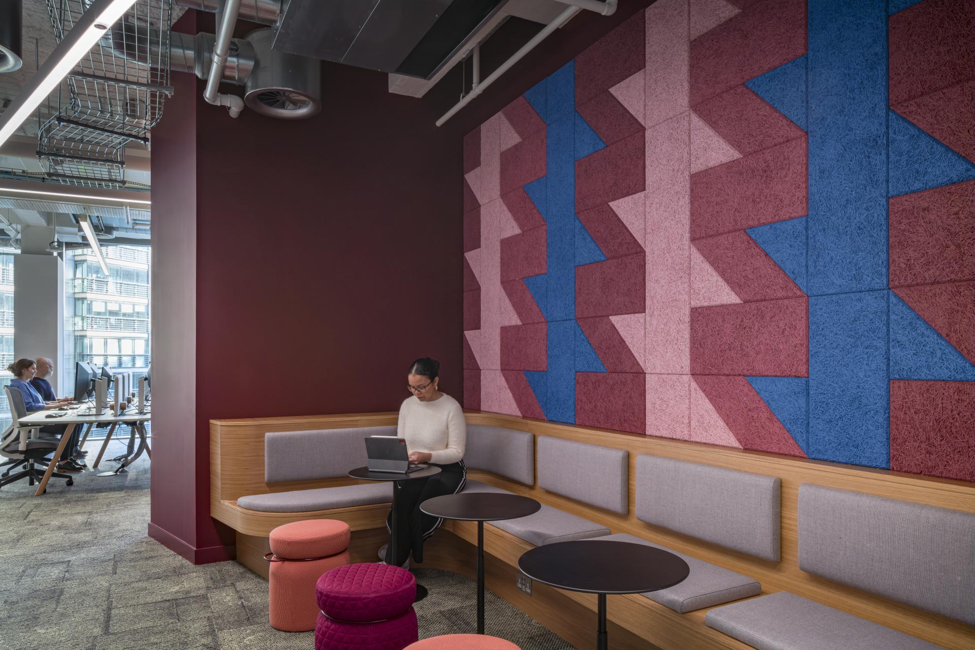 Modern workspace in Virgin Media O2 headquarters featuring vibrant wall design, comfortable seating, and a focused professional using a laptop.