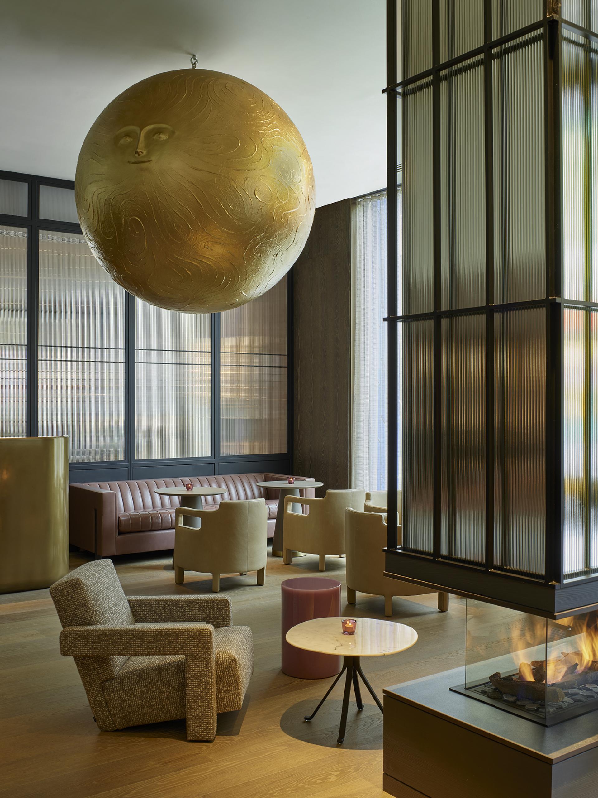 Luxurious hotel lobby in Leicester Square featuring a gold globe artwork, modern seating, and a contemporary fireplace.