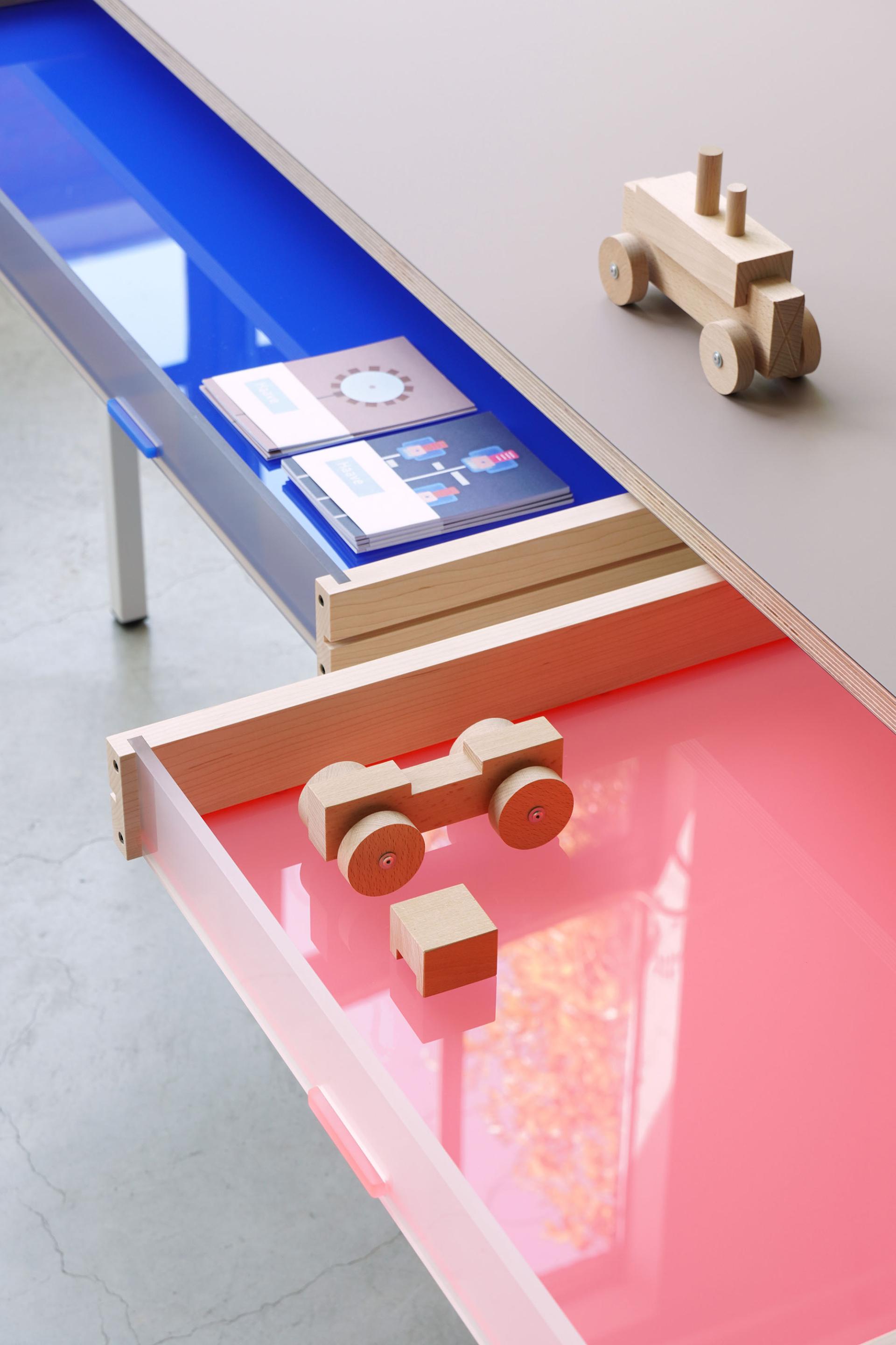 A close-up of a colorful modern table displaying wooden toys and design brochures, illustrating innovative design concepts from DDW 2023.