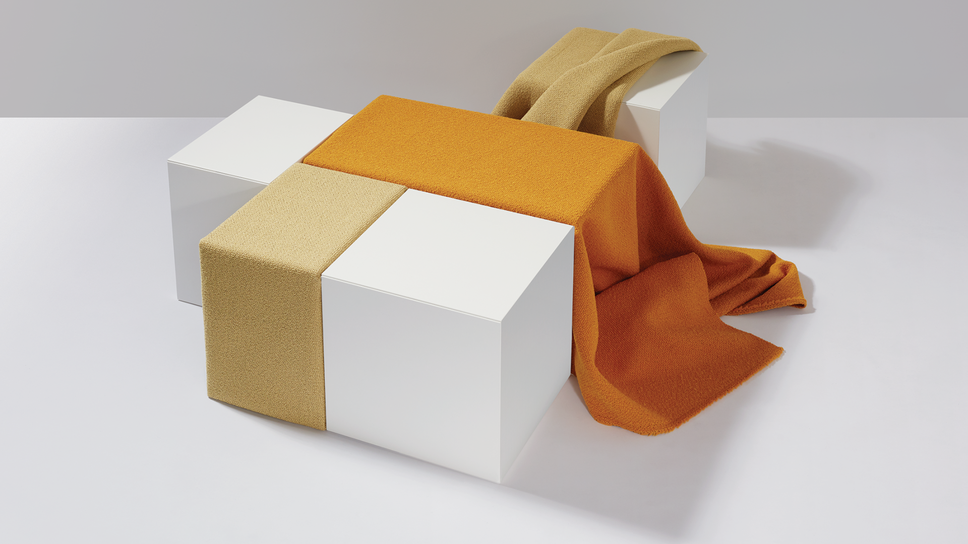 Textiles in earthy tones draped over minimalist white blocks, showcasing sustainable British manufacturing by Camira.