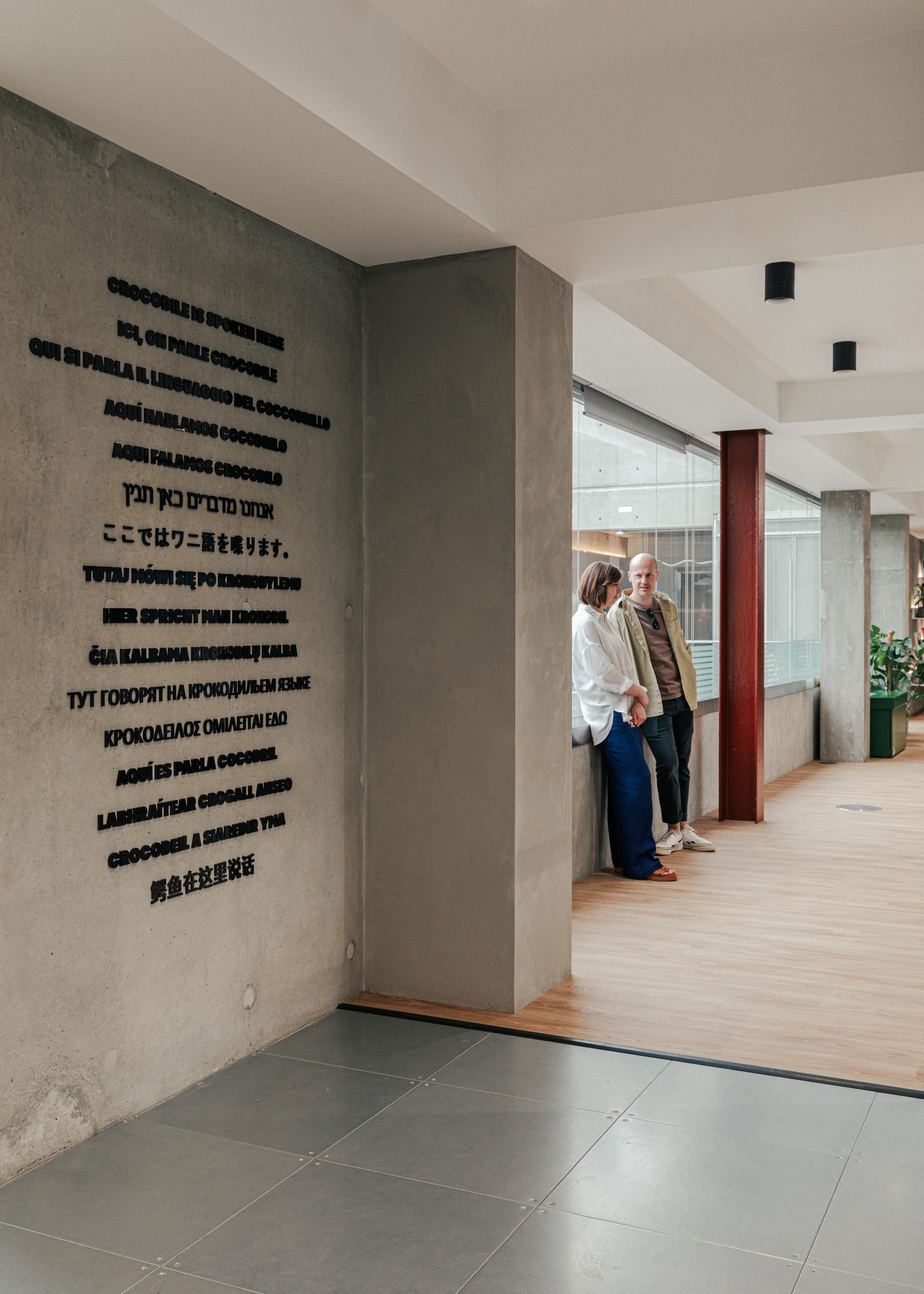 Contemporary workspace featuring a concrete wall with multilingual text, reflecting Lacoste's New York warehouse-inspired design.