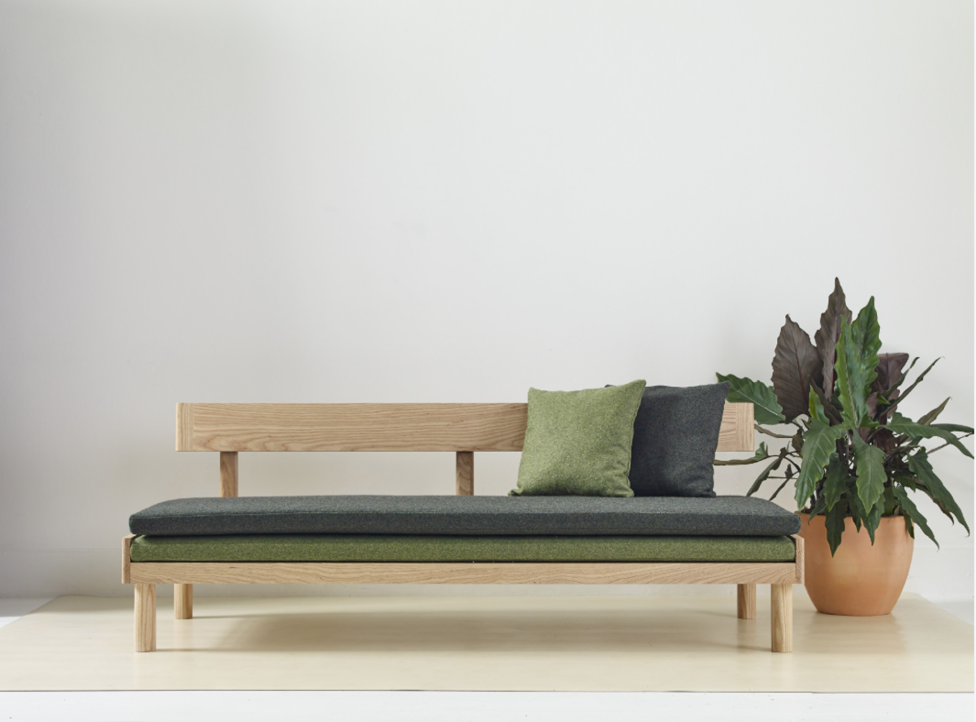 Modern wooden bench with green and gray cushions, complemented by a potted plant, designed for wellbeing aesthetics.